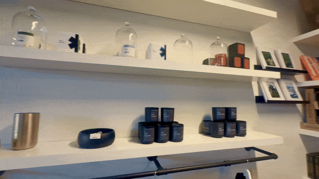 White shelves displaying glass domes, black and orange boxes, small black containers, a silver cylindrical item, framed pictures, and books on the right side.