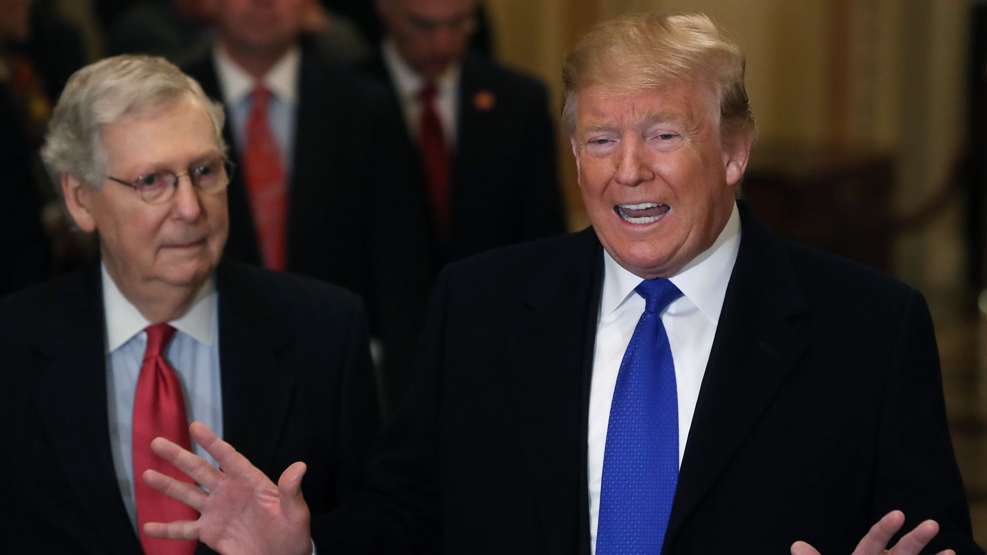 In this image, Mitch McConnell stands next to President Trump, who is talking with both hands splayed out in front of him.
