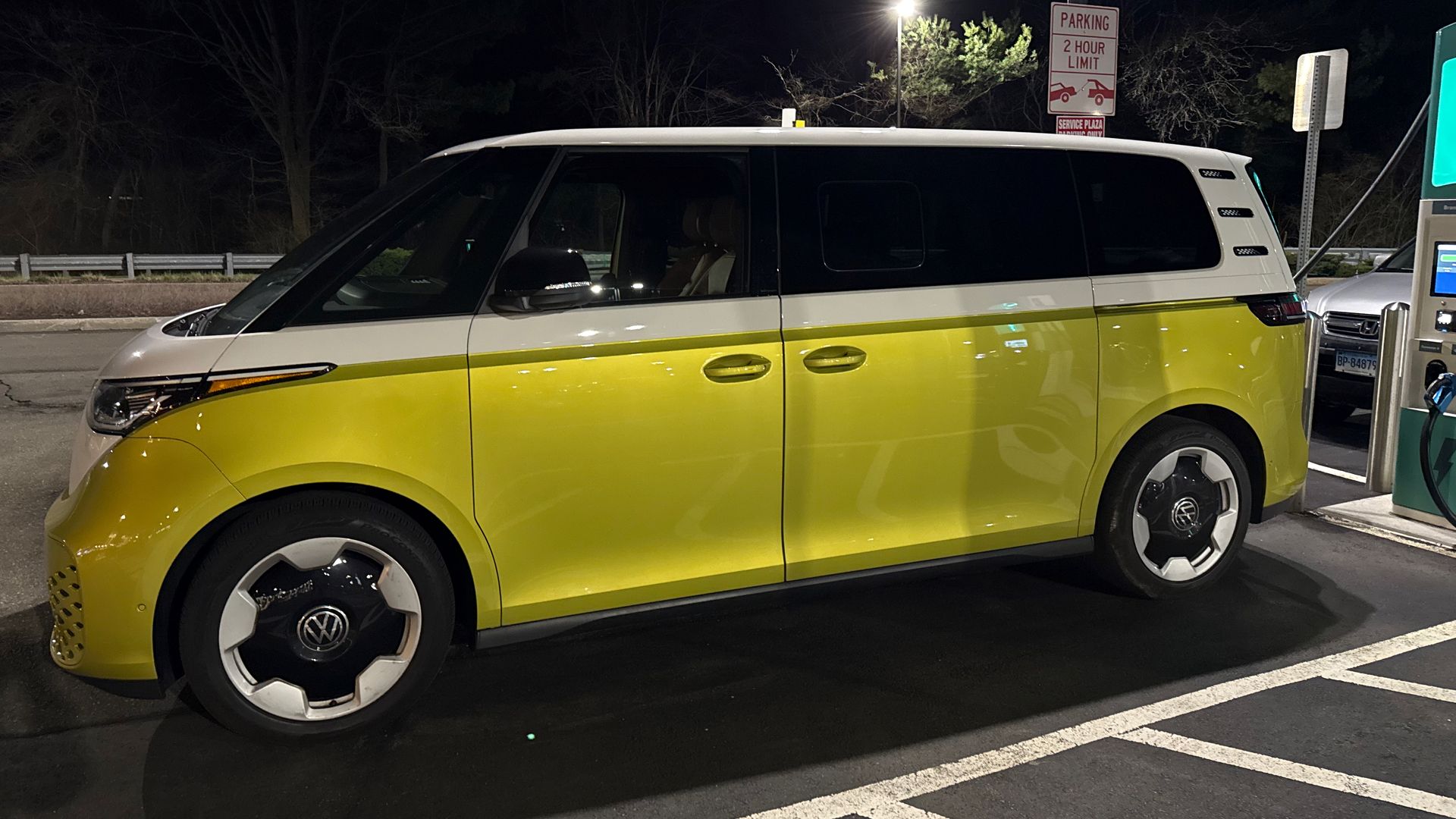 An two-tone VW ID.Buzz electric van — white and electric yellow — charges at night in a New Jersey travel plaza.