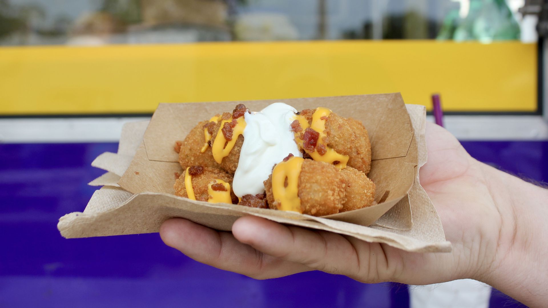 A photo of a hand holding up a paper tray of two loaded crab bites drizzled in cheese and sour cream.