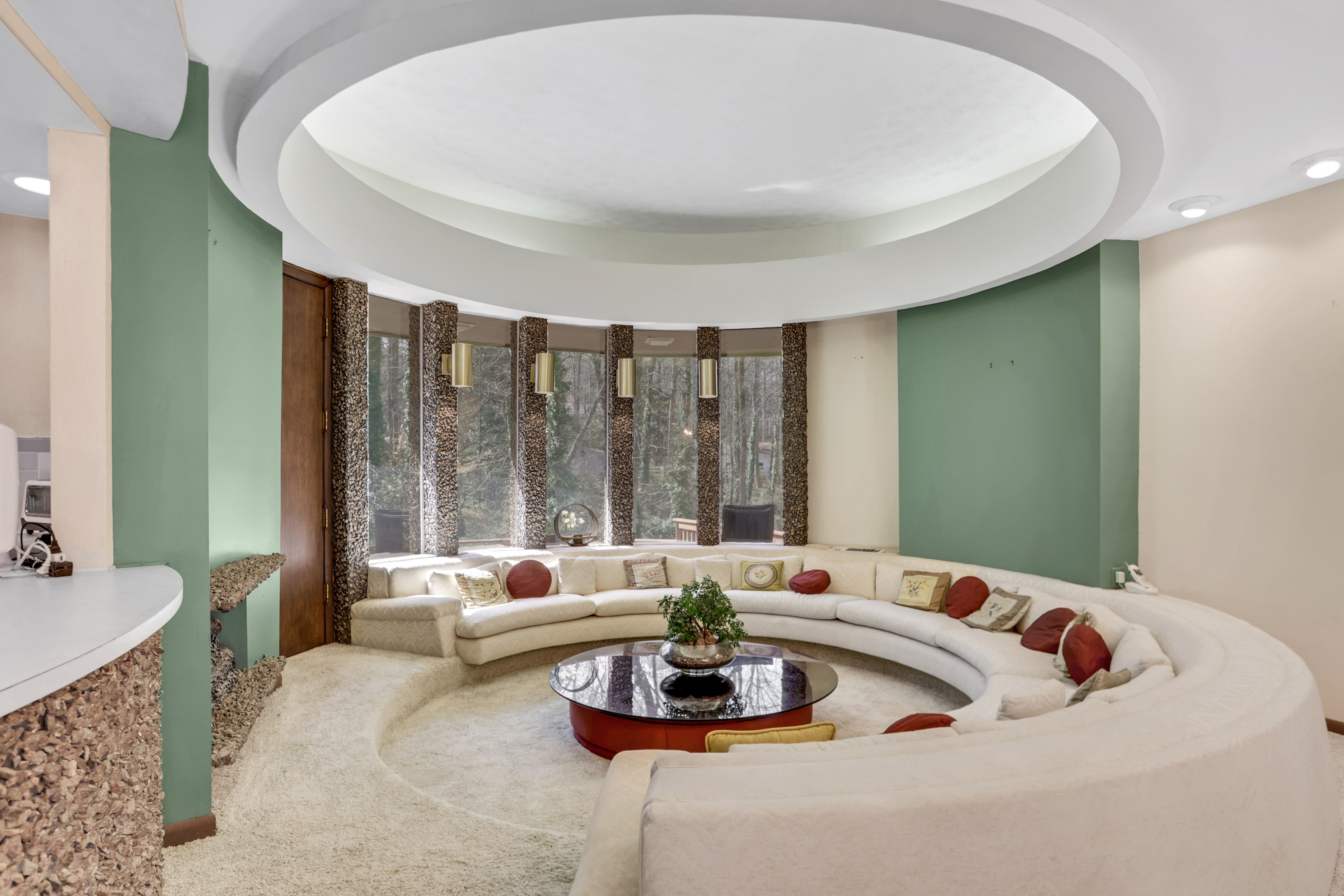A conversation pit with a large circular ceiling feature overhead and aqua walls