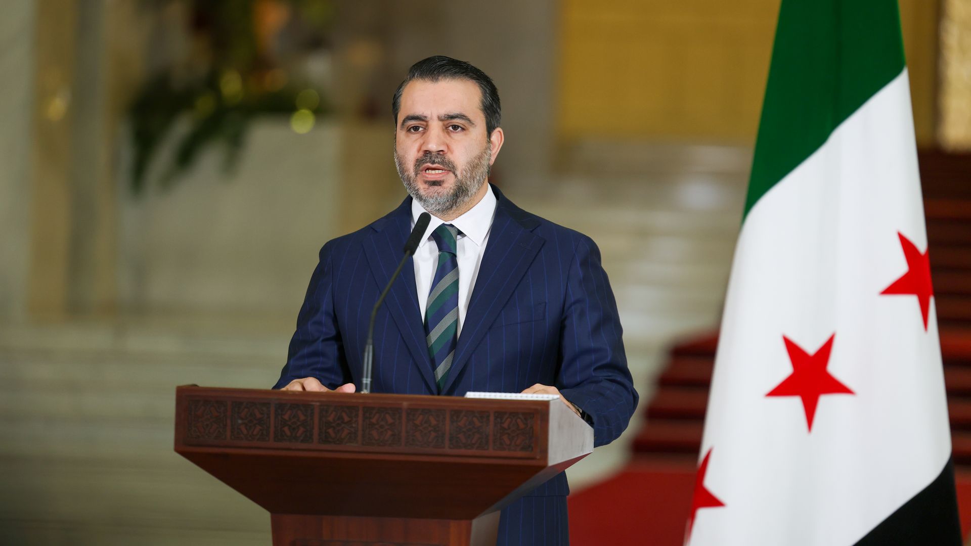 Man in suit before syrian flag