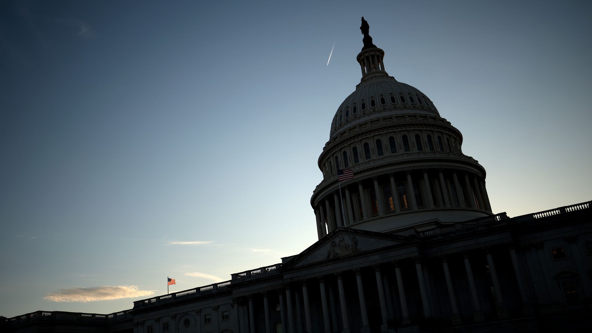 The U.S. Capitol, tinted by a shadow against the backdrop of a sunset sky.