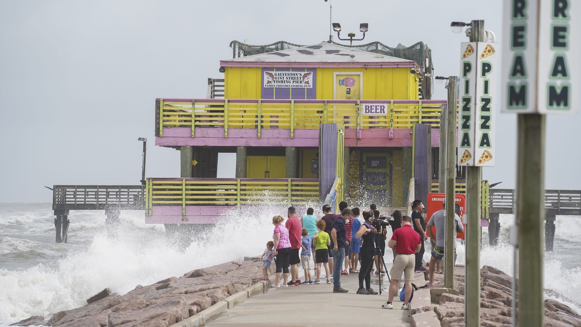 People stand at a pier to watch high waves ahead of Hurricane Laura in Galveston