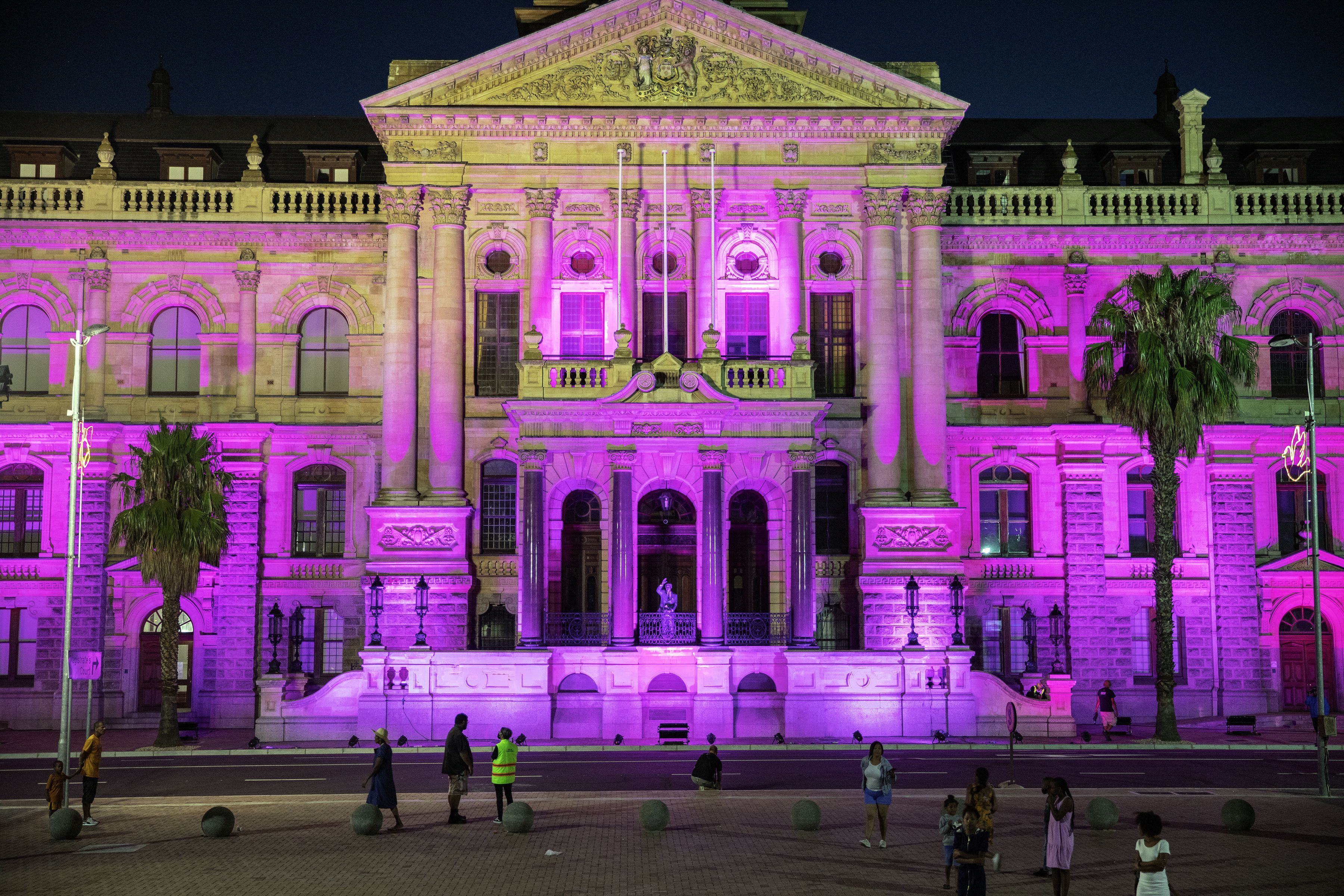 Bystanders walk past the Cape Town City Hall litten in purple at night to honour South African anti-apartheid icon Archbishop Desmond Tutu following his death