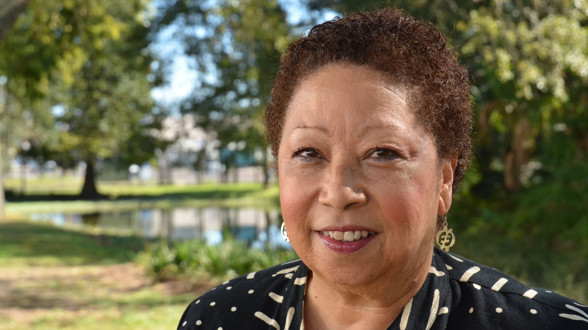 In a formal headshot, Mona Lisa Saloy smiles as she looks directly at the camera. A park can be seen in the background.