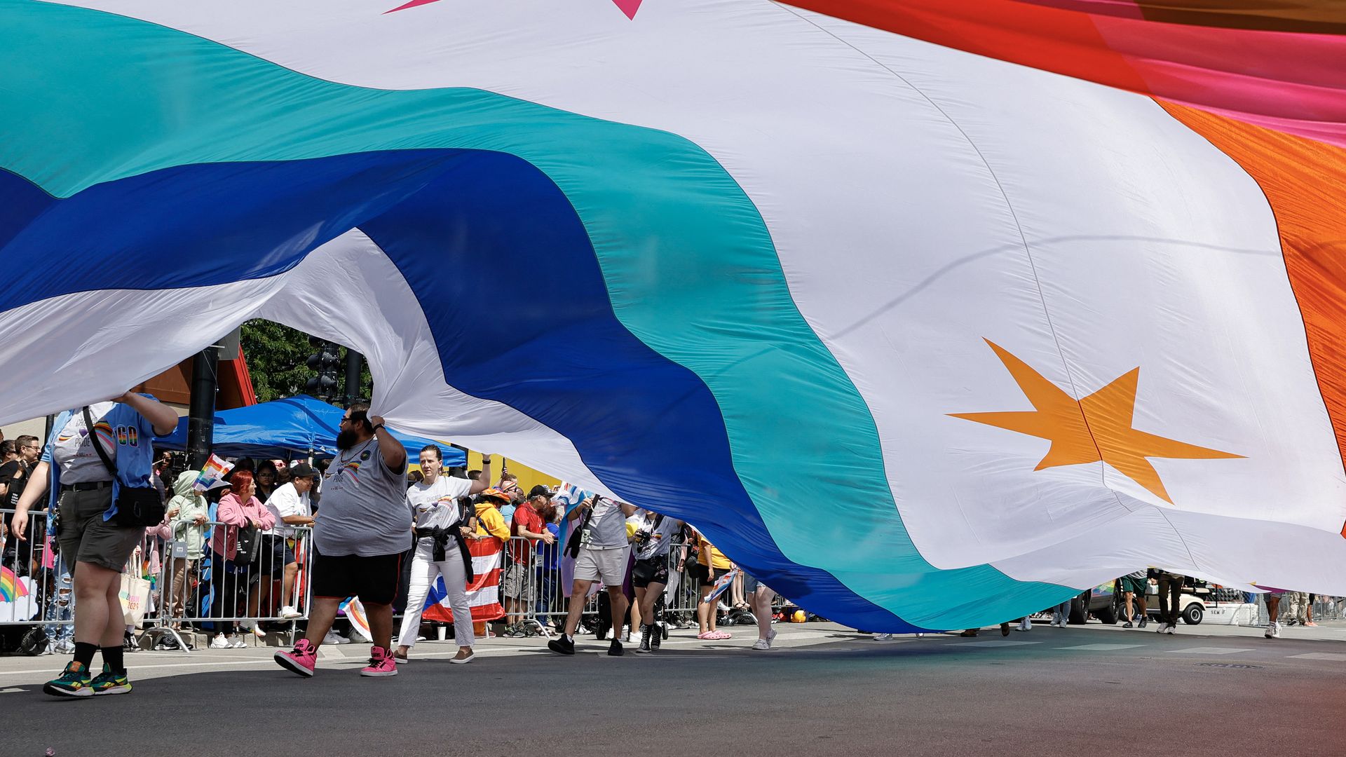 Photo of a parade with a huge flag being carried.