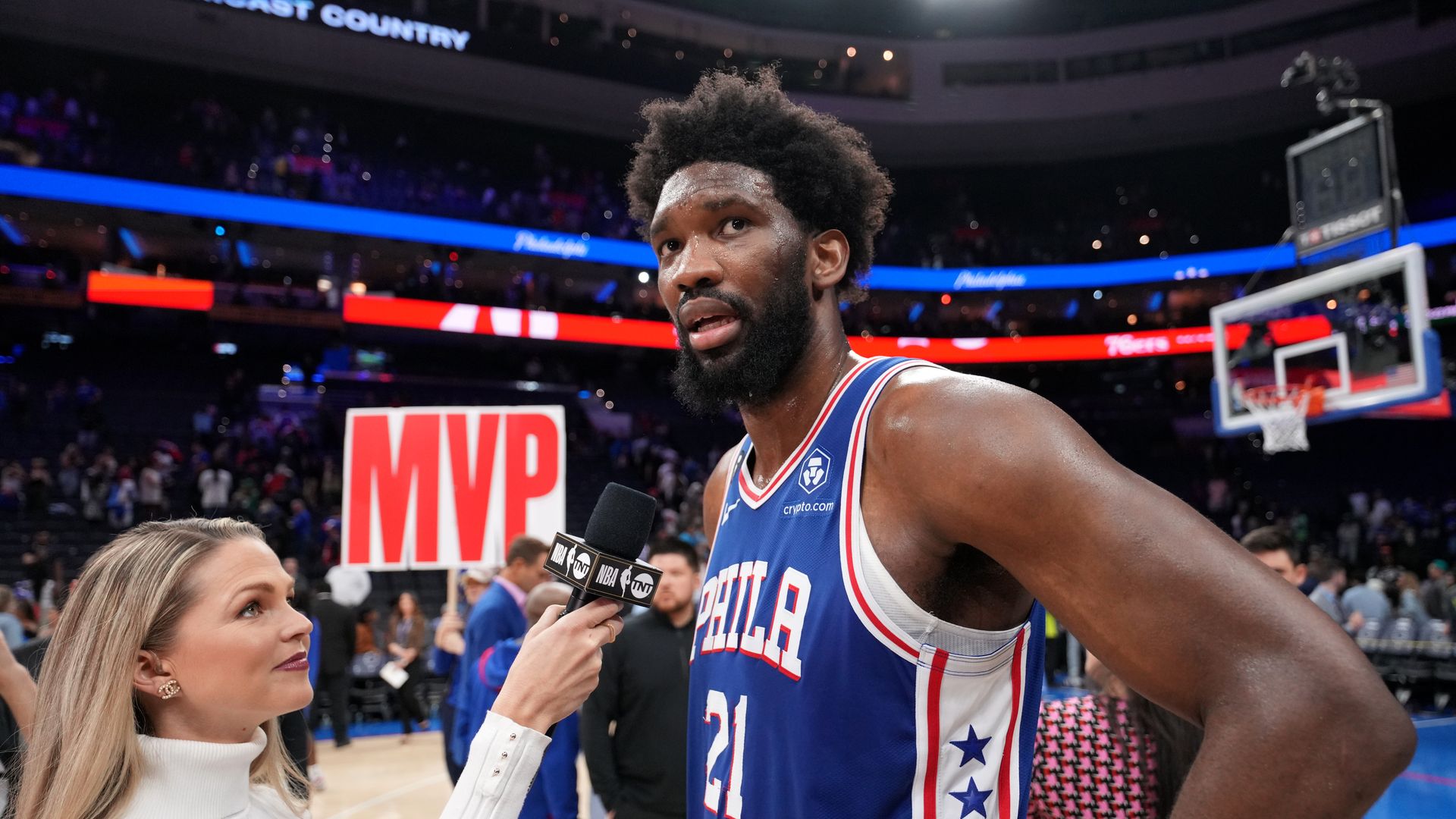 Sixers center Joel Embiid being interviewed courtside by a reporter.