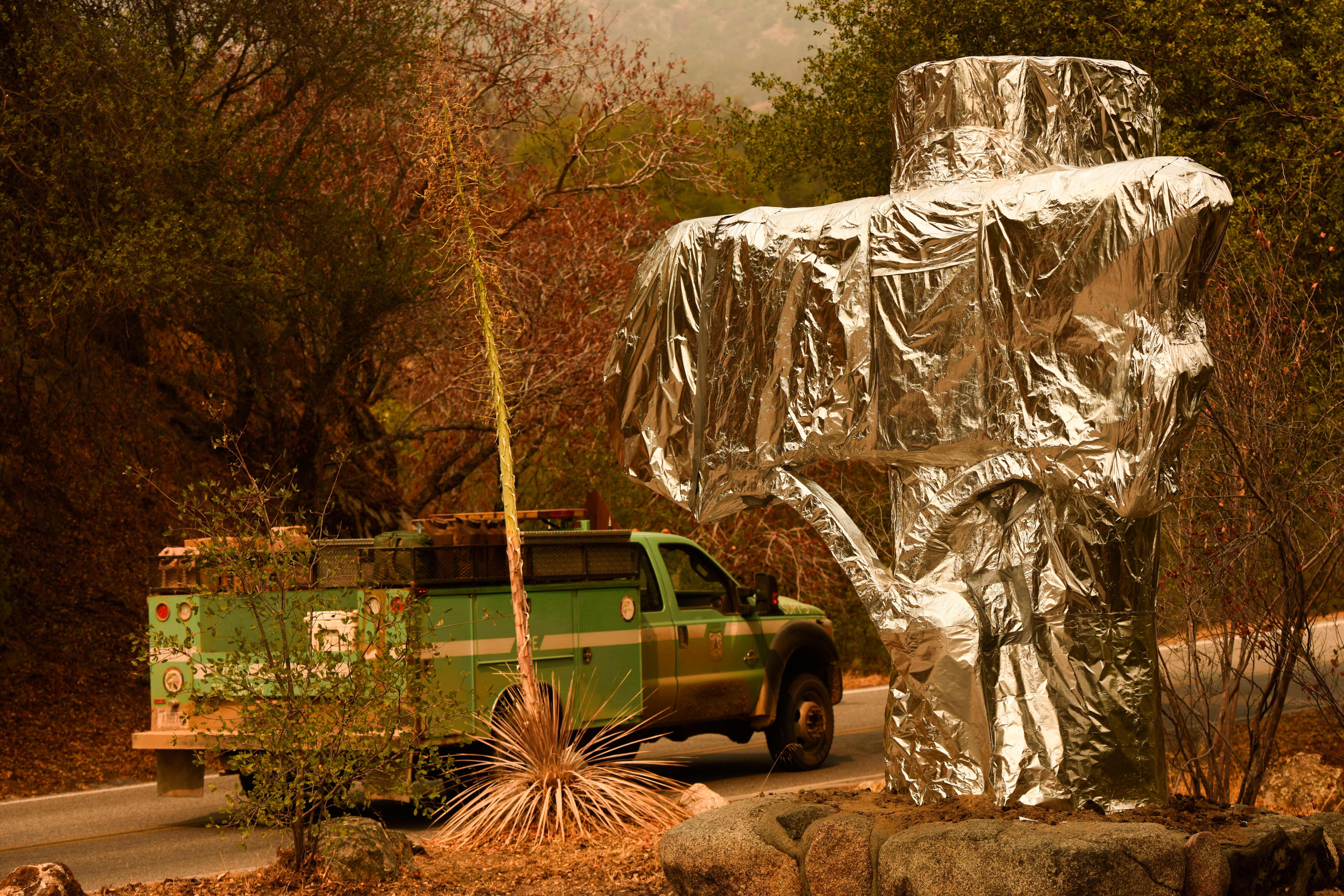 A US Forest Service vehicle drives past the Sequoia National Park historic park entrance sign wrapped in fire resistant foil in California