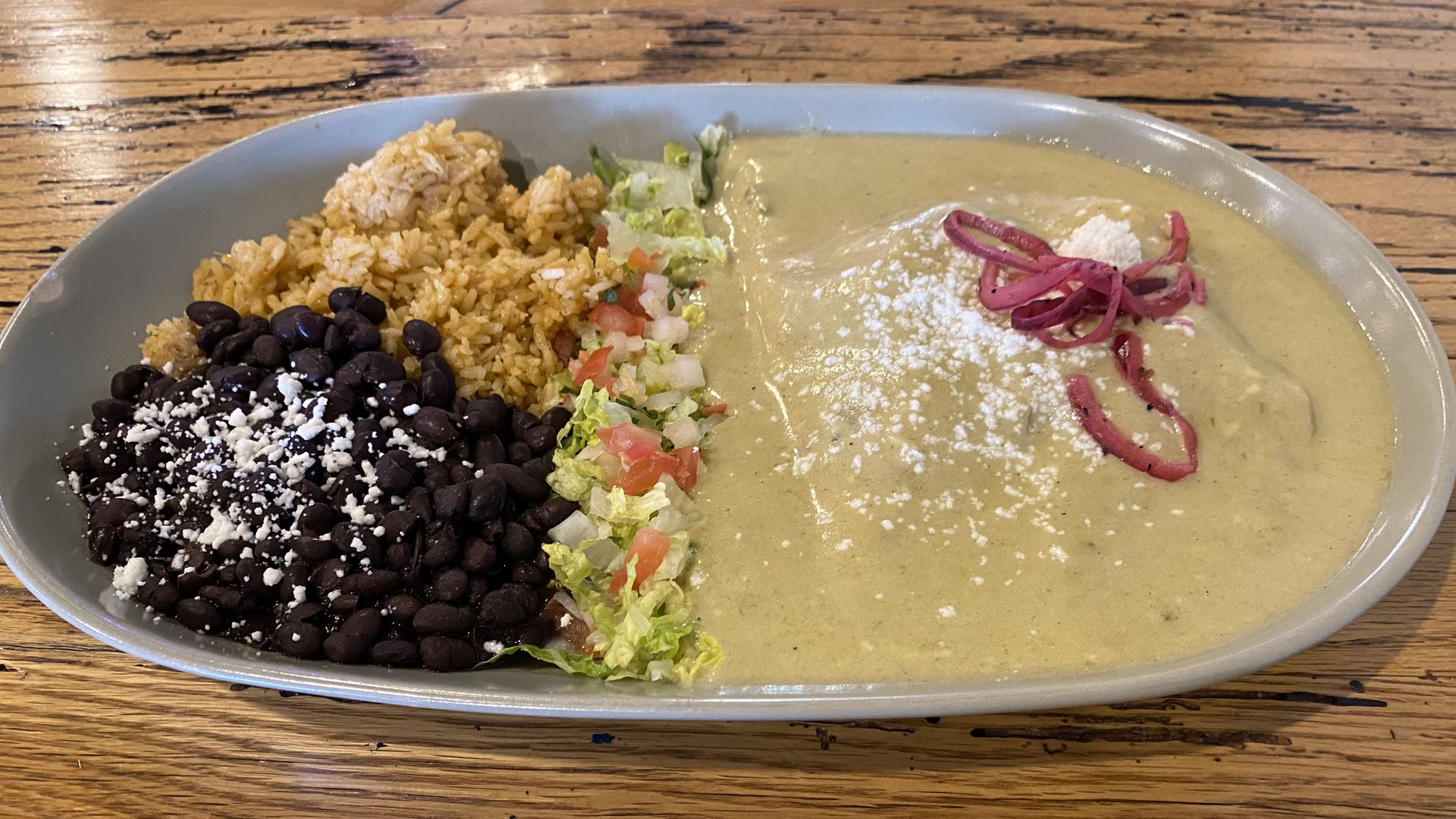 A plate with black beans and rice on one side and enchiladas covered in green sauce on the other.