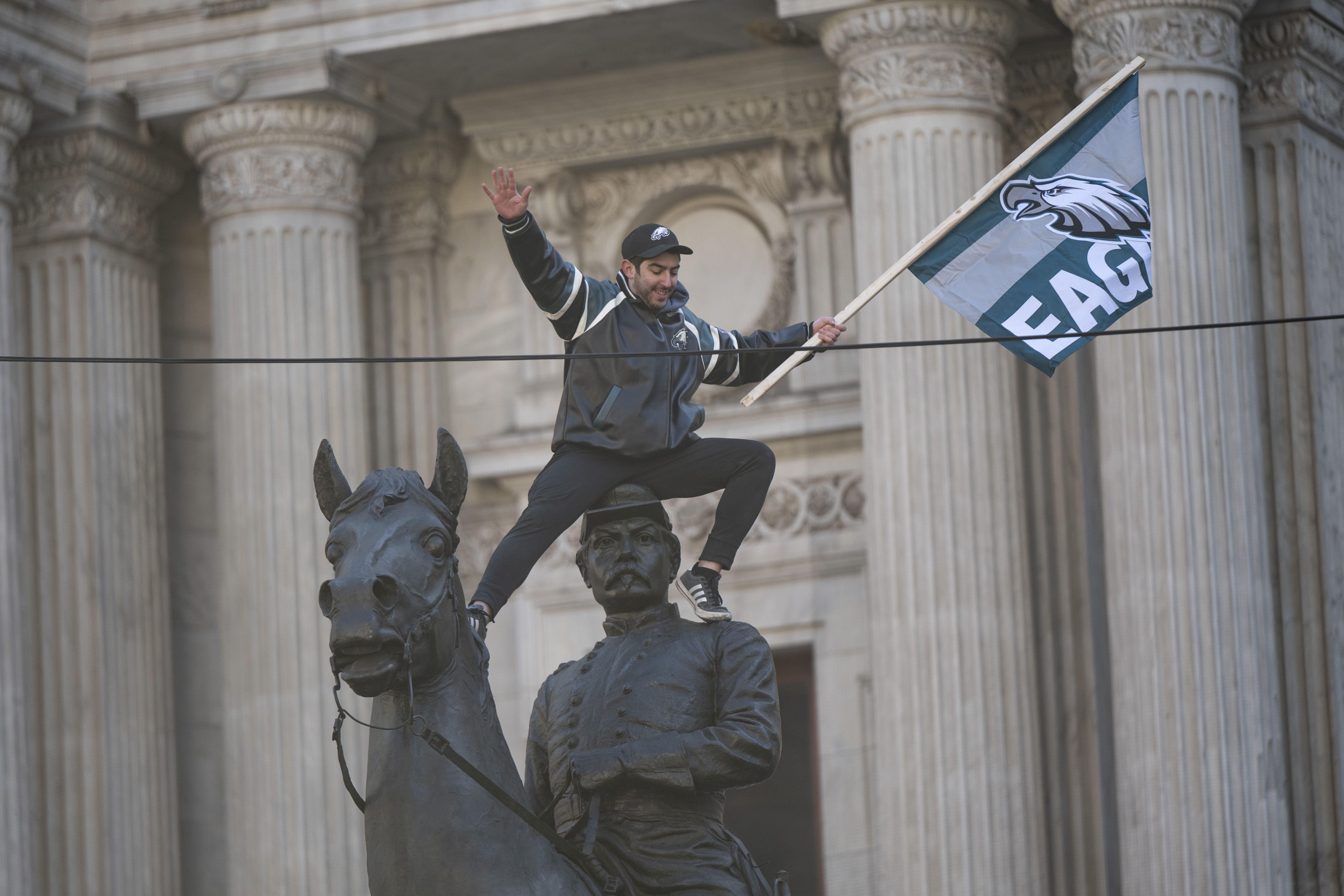 A man sits on top of a statue waving an Eagles flag