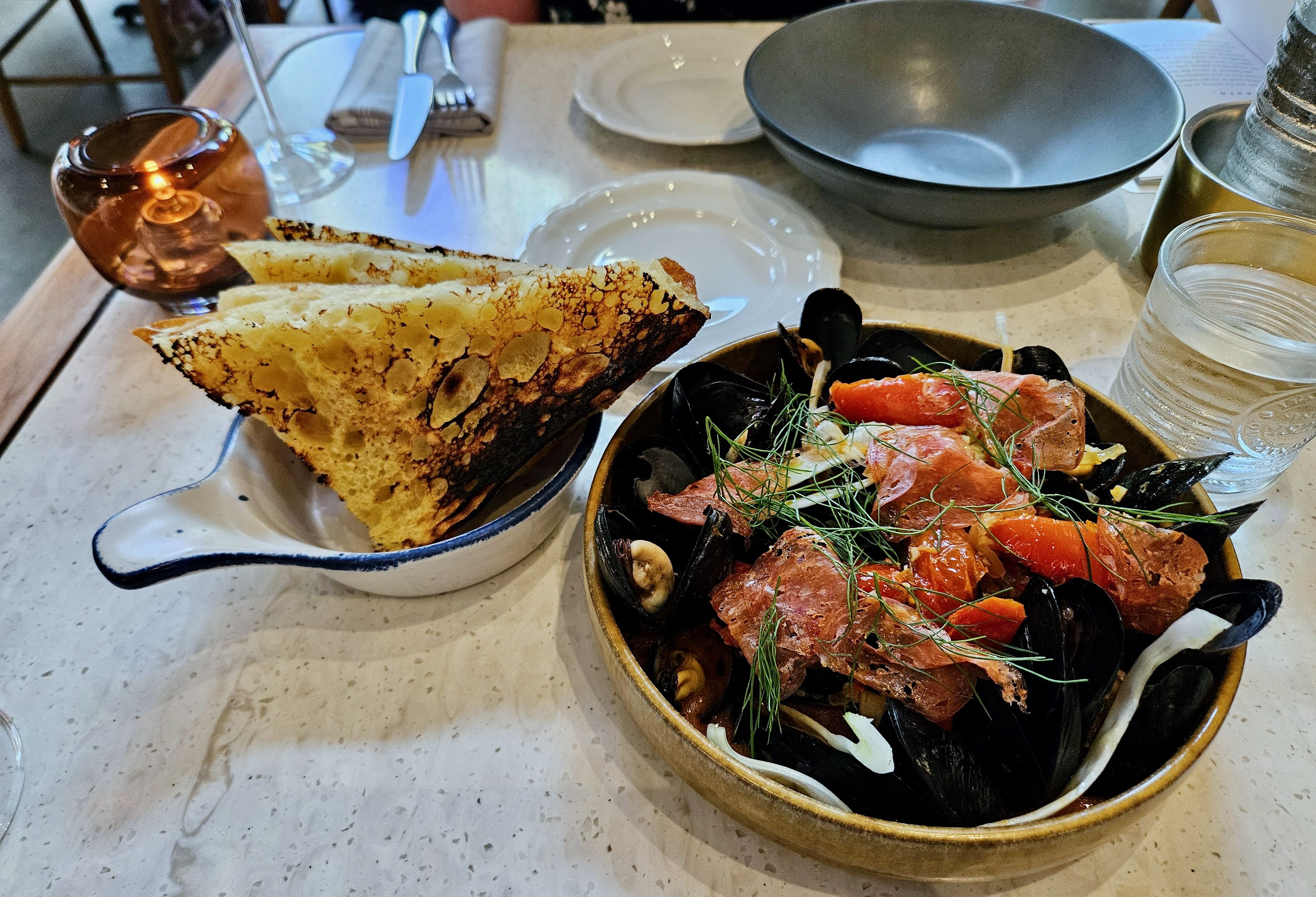 The mussels, topped with salami, in a pan next to a bowl of scacciata bread