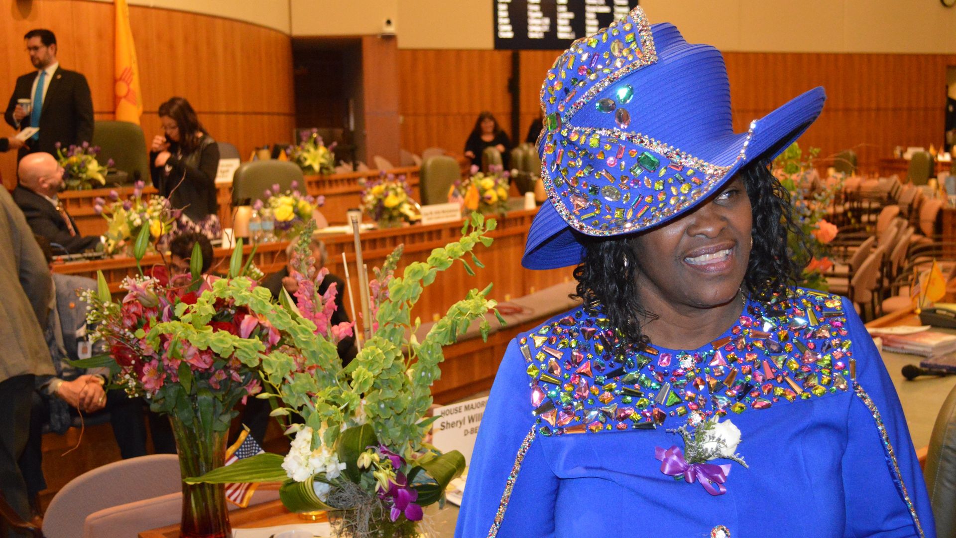 Democratic New Mexico state lammaker Sheryl Williams Stapleton stands on the New Mexico House floor with a blue hat. 