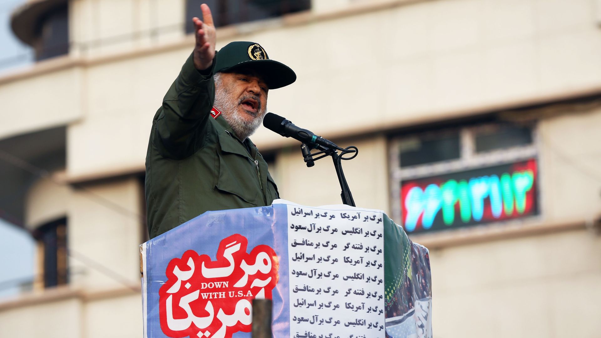 In this image, a man in a military uniform and hat stands at a podium with the words "Down with the USA" written on the side.