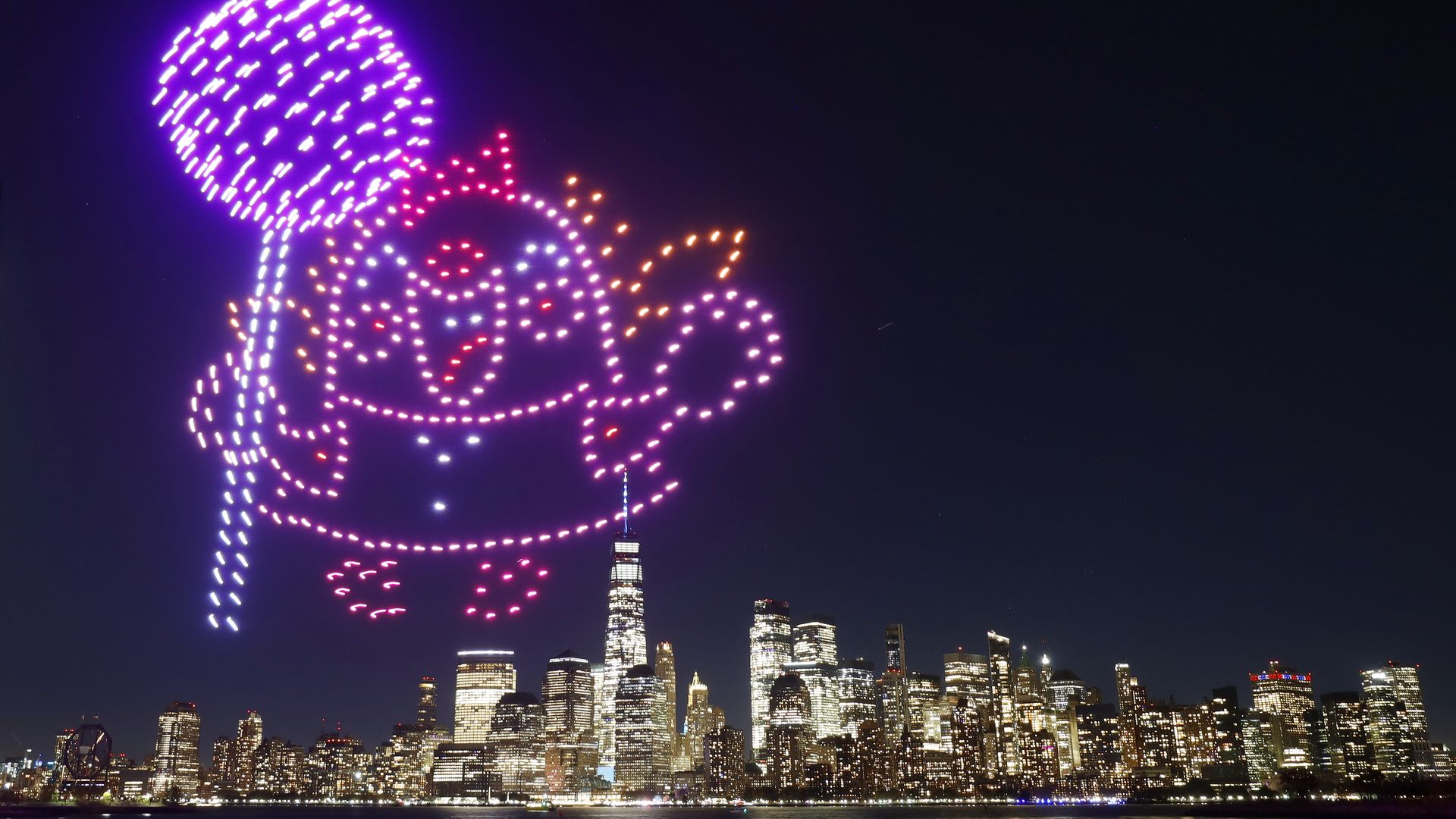 A character holding a lollipop is created by 500 drones over the skyline of lower Manhattan and One World Trade Center.