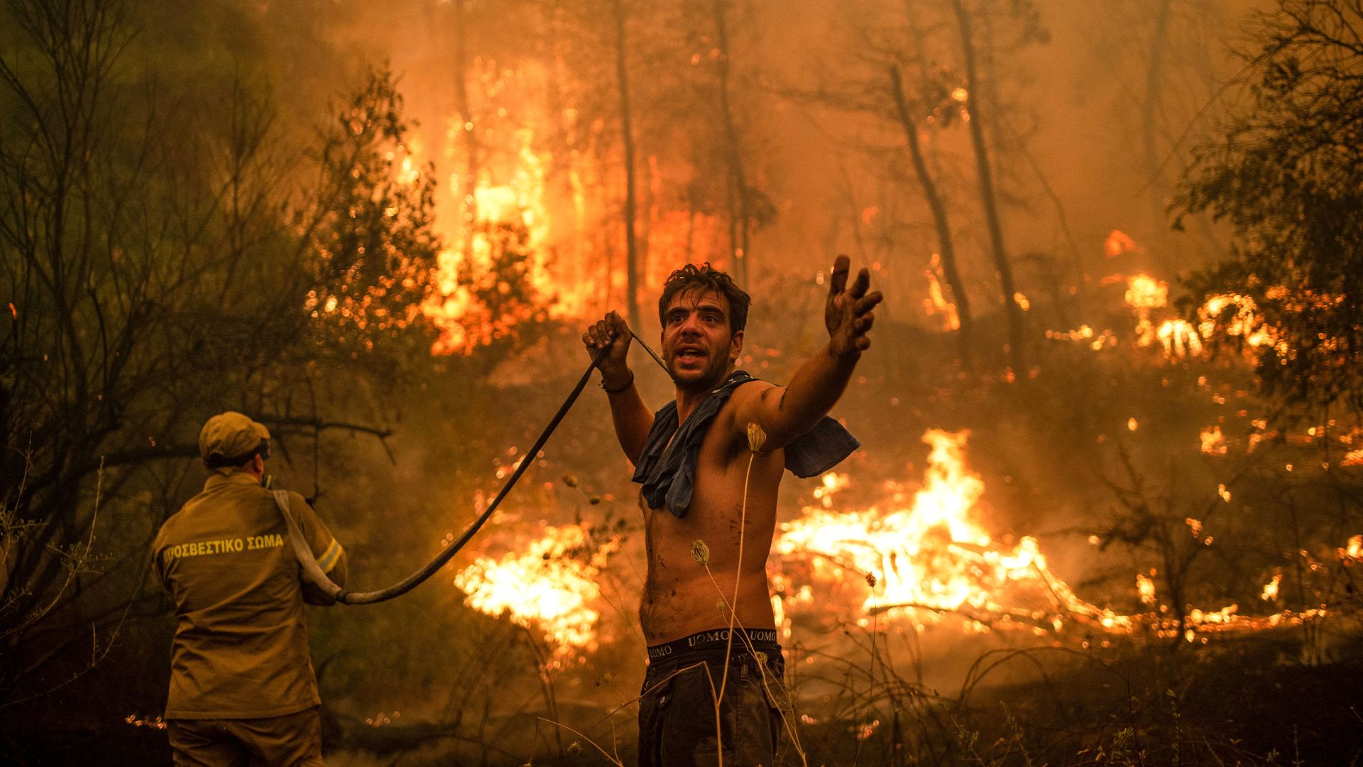 A local resident gestures as he holds an empty water hose during an attempt to extinguish forest fires approaching the village of Pefki on Evia (Euboea) island in Greece.