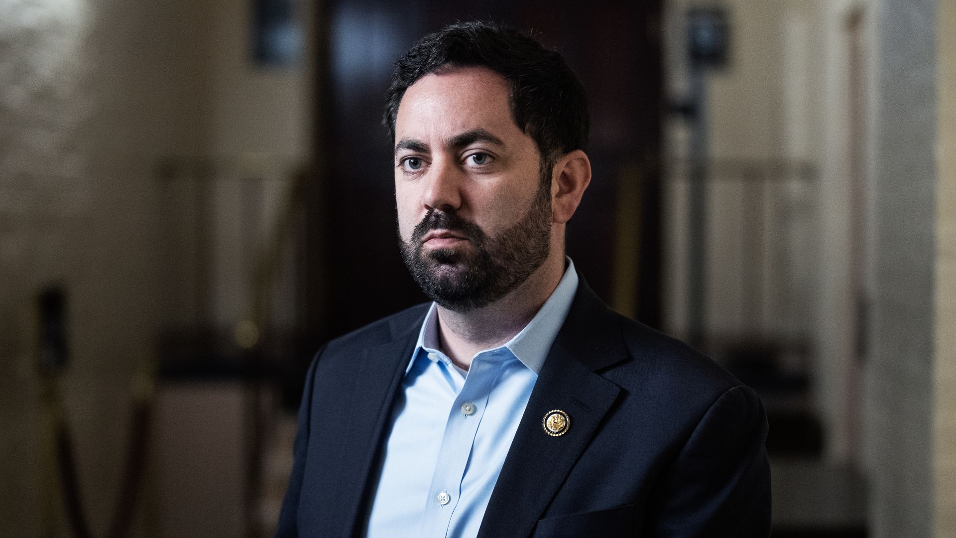 Rep. Mike Lawler (R-N.Y.), with dark hair and beard wearing a navy suit jacket and light blue shirt, standing indoors with a serious expression and a gold circular pin on his jacket lapel.