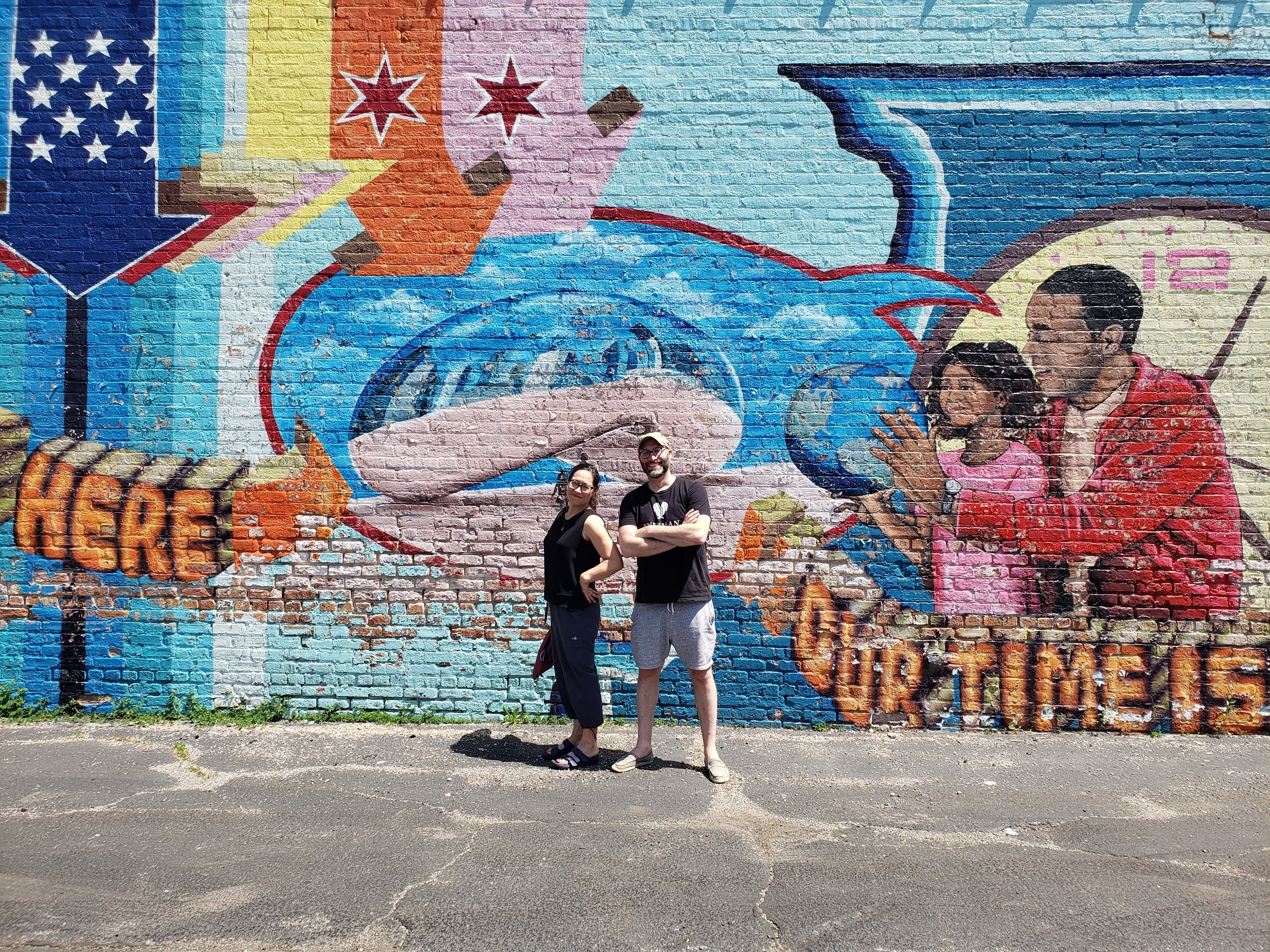 Photo of two people posing in front of a mural. 