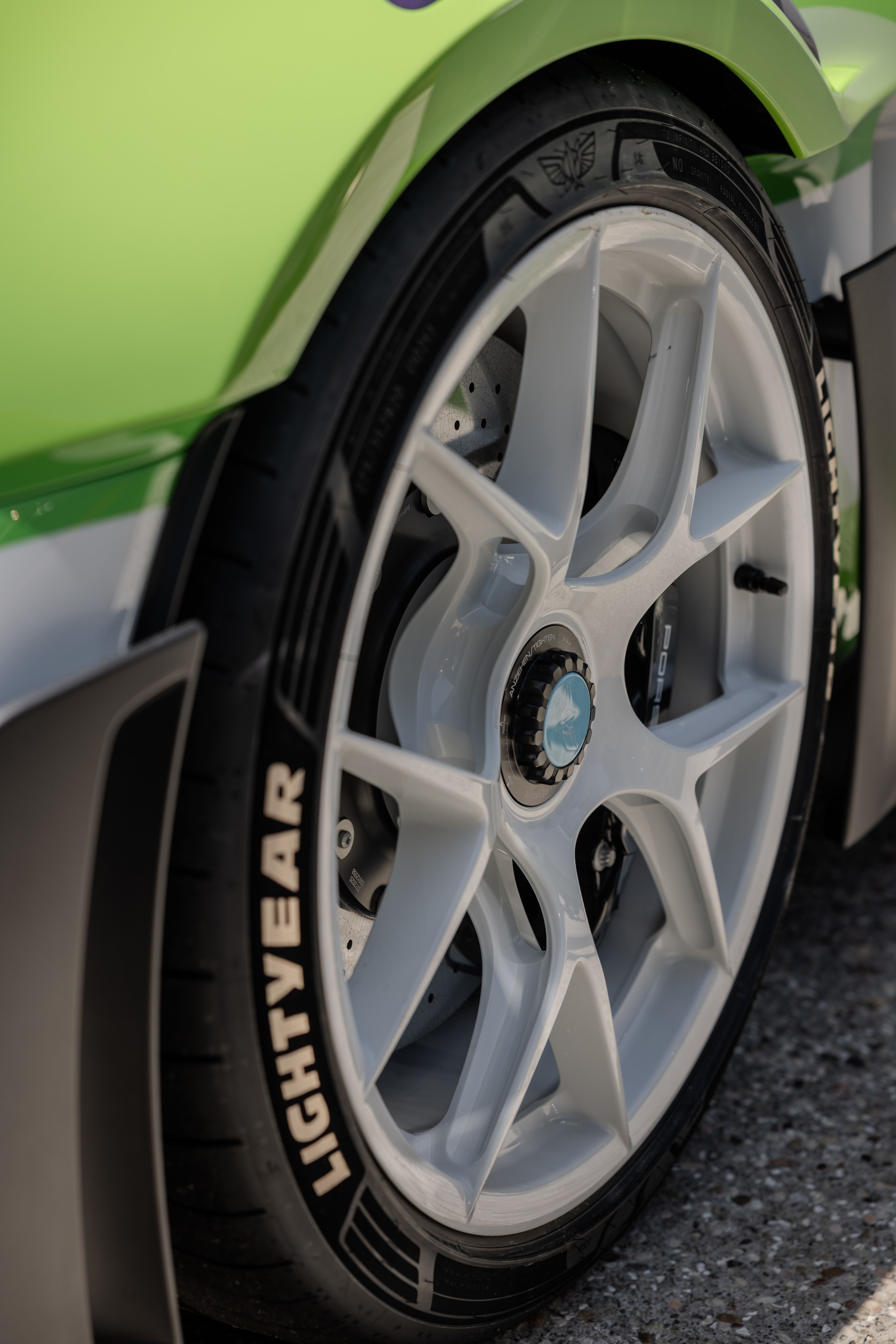 Close-up of a lime-green sports car wheel: large silver alloy rim, visible brake rotor, and black tire with white lettering; glossy green body panel above.