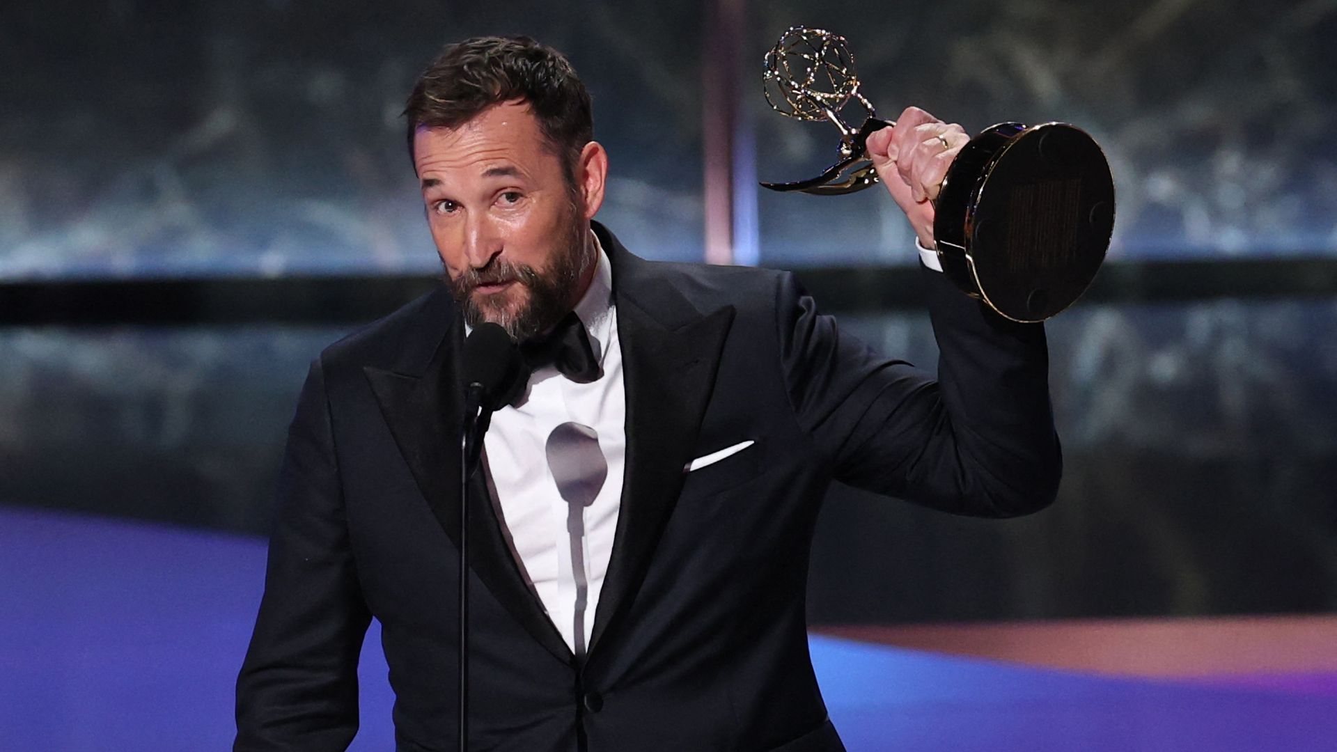 Actor Noah Wyle accepts his Emmy win in a black and white tuxedo, holding an Emmy award. 