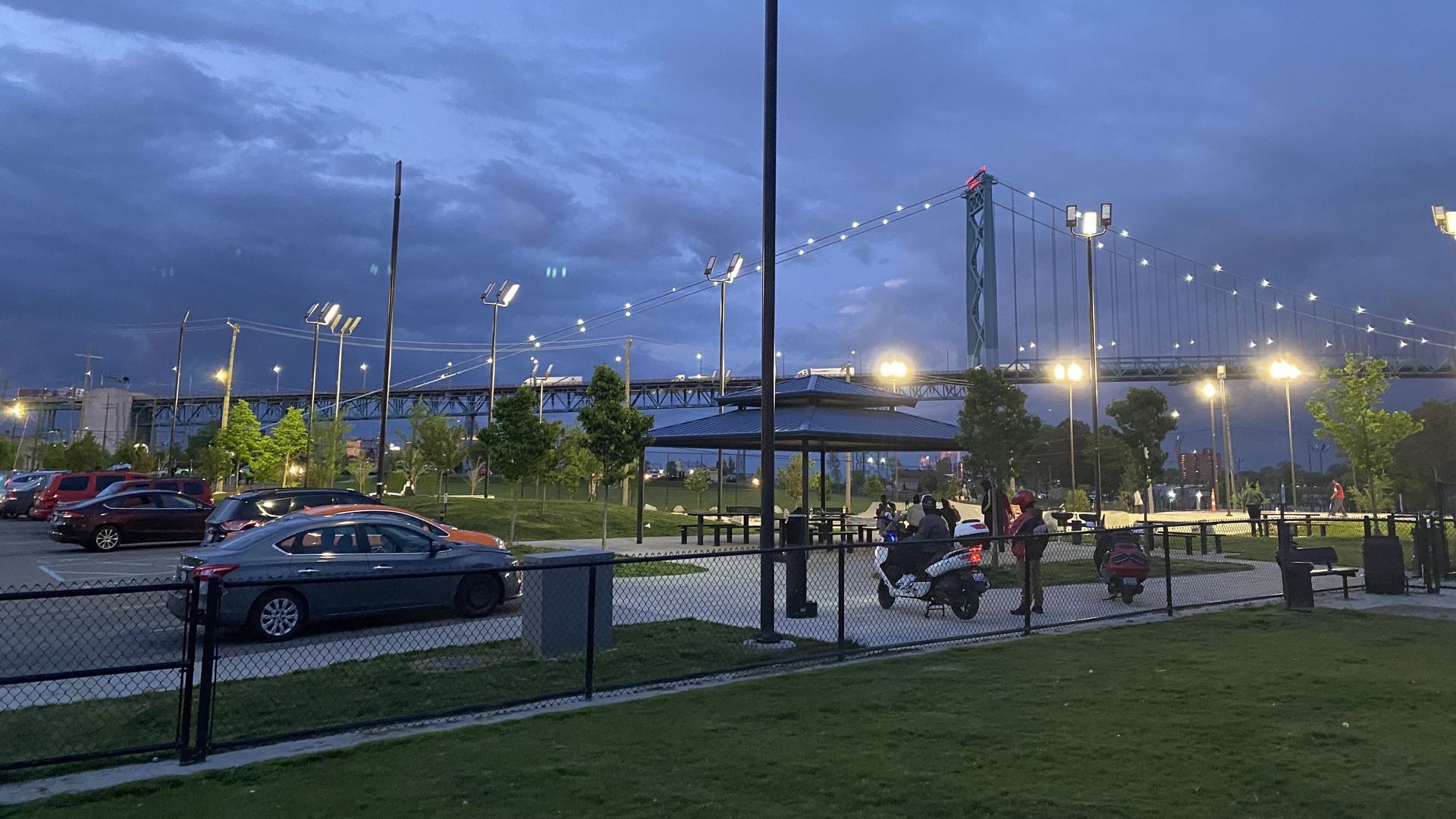 People hang out at a skate park at night, with the Ambassador Bridge visible in the background.