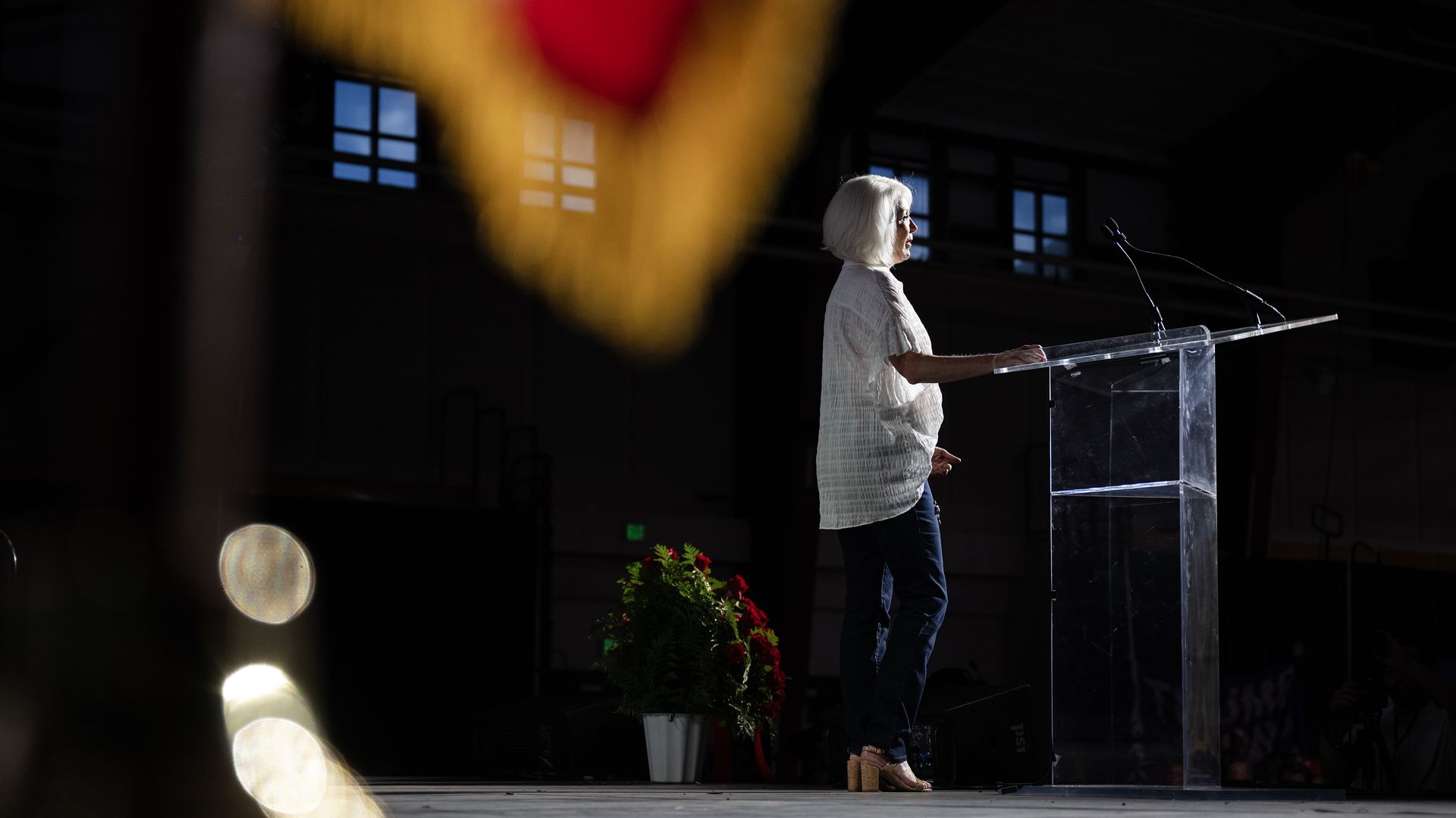 An image of Tina Peters in the distance while standing on stage at a podium.