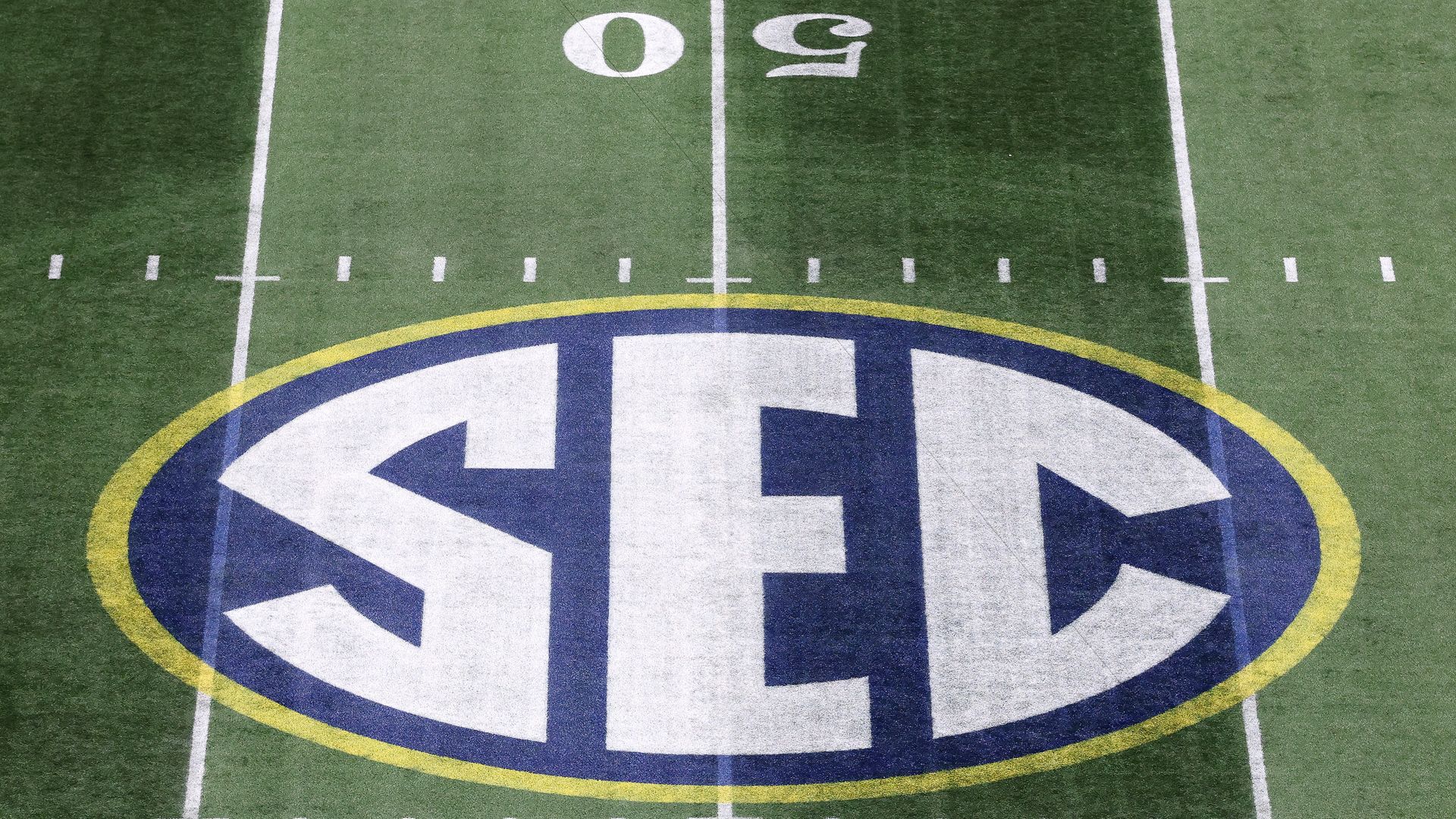 The "SEC" logo on on a football field near the 50 yard line, artificial turf with white lines and "50" visible as well.