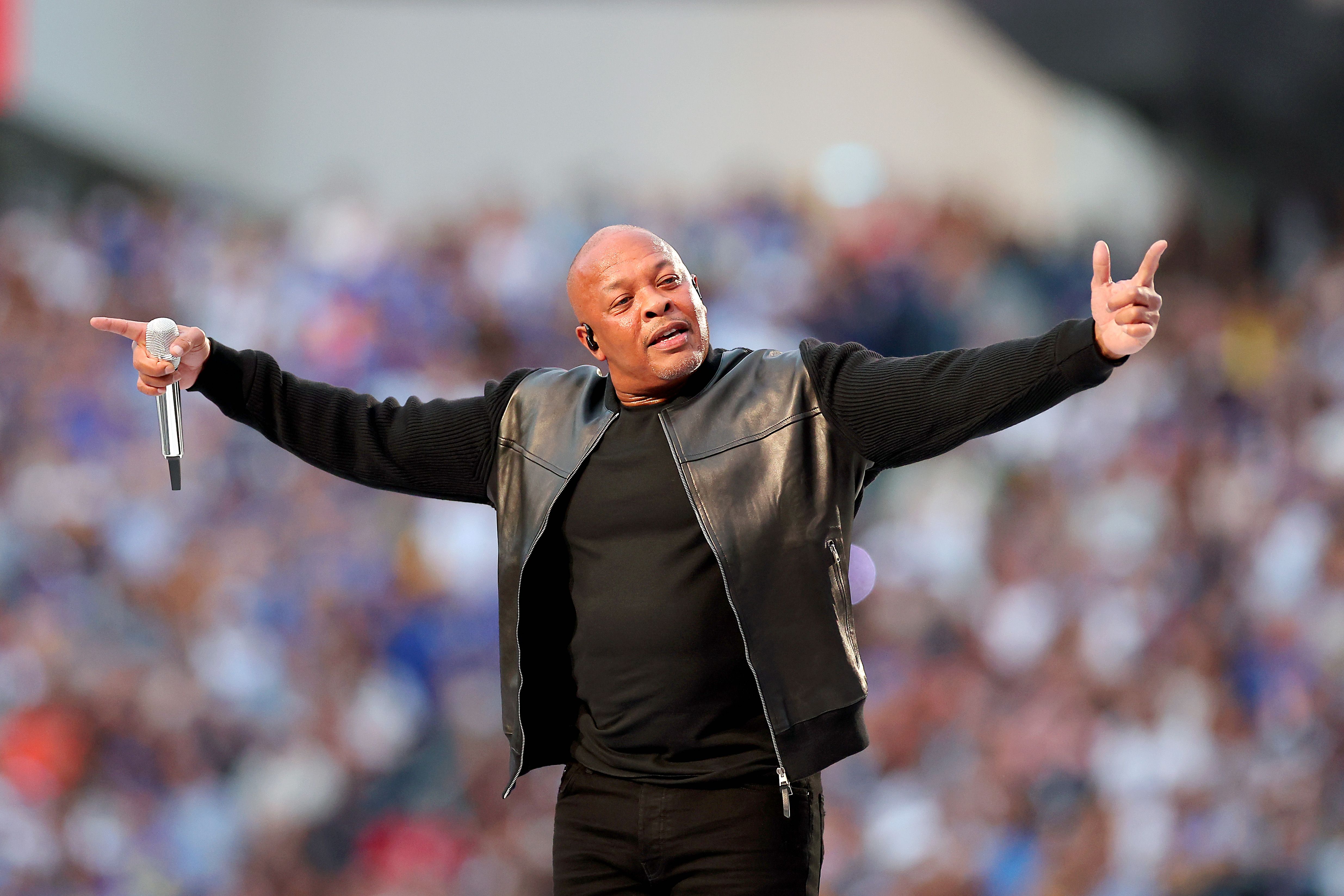 Music icon Dr. Dre performs on stage at the Super Bowl with his arms stretched out.