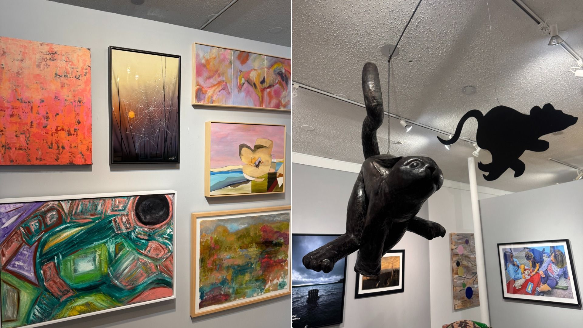 Gallery wall with colorful abstract paintings and a framed photograph, a large black cat sculpture suspended from ceiling, and a black silhouette of a mouse also hanging from ceiling.