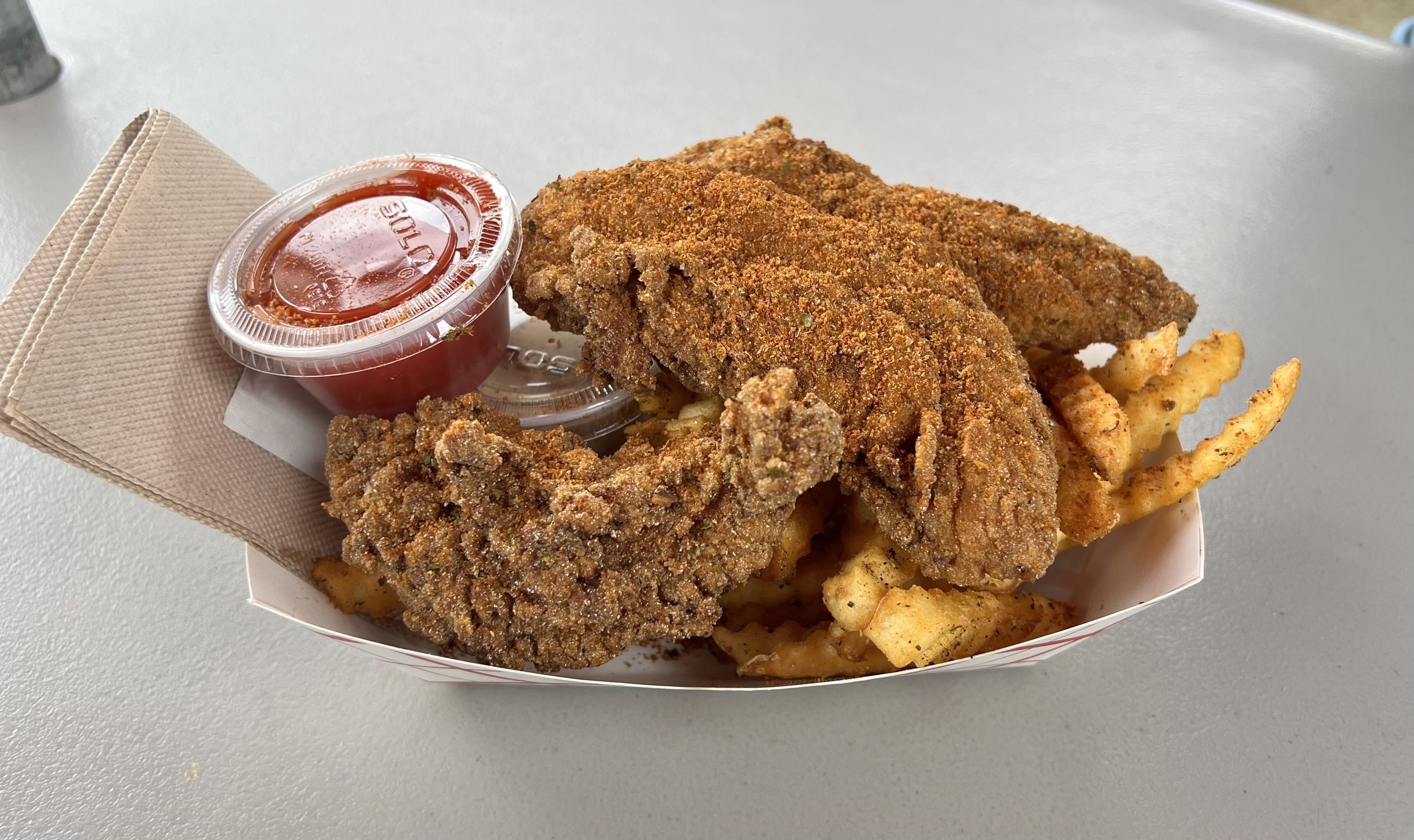 A photo of chicken tenders on a paper plate with a red sauce.
