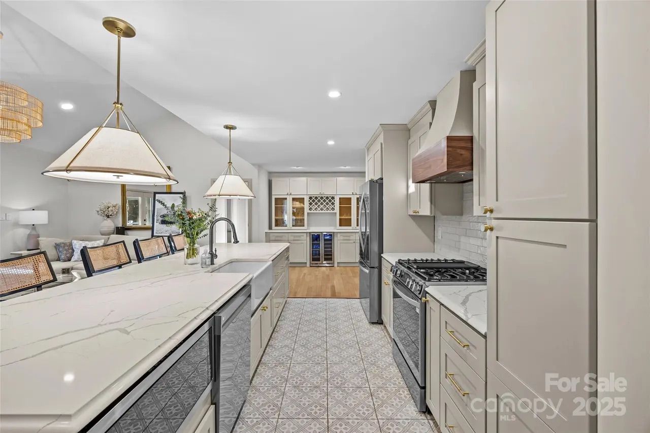 Modern kitchen with beige cabinetry, white marble countertops, a patterned tile floor, stainless steel appliances, pendant lights, and a vase of flowers on the island.