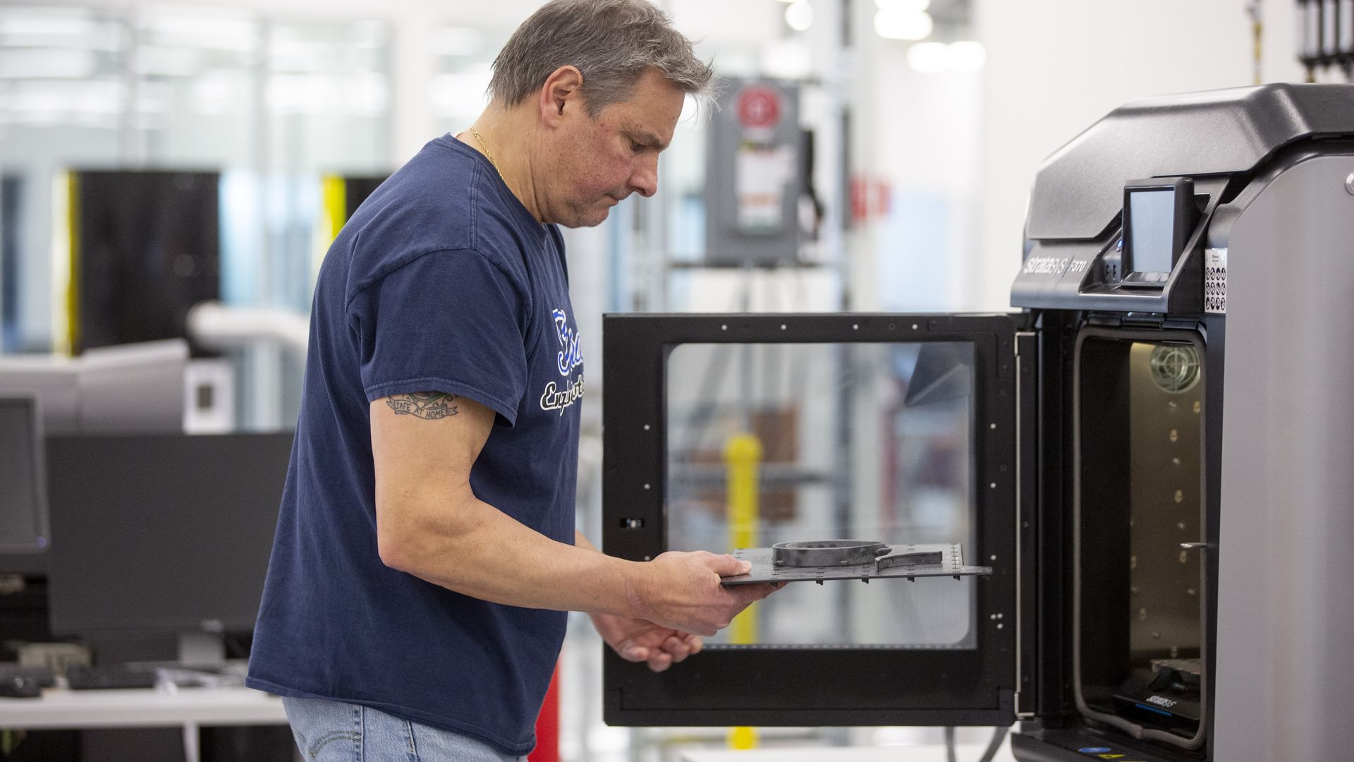 A Ford worker removes medical face shield parts from a 3D printer.  