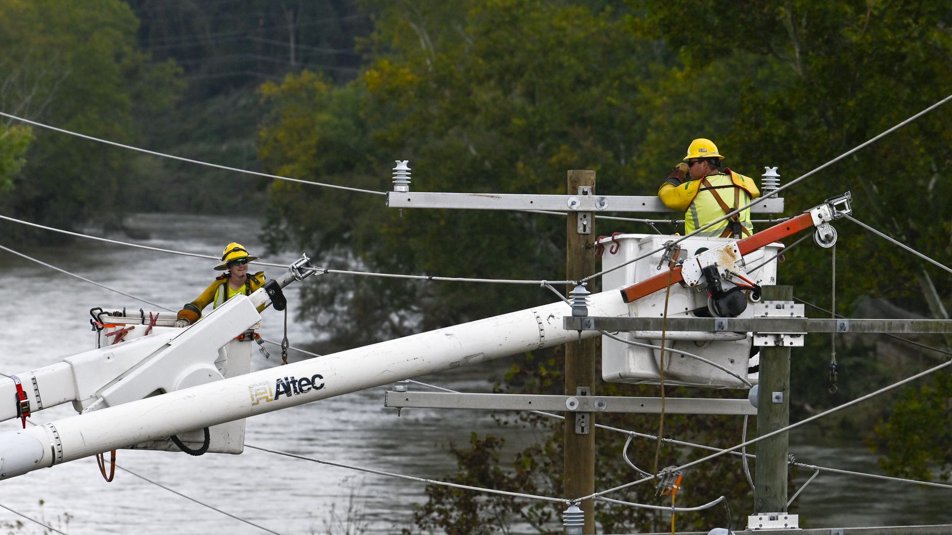 Photo showing workers repairing power lines while attached to buckets from trucks. 