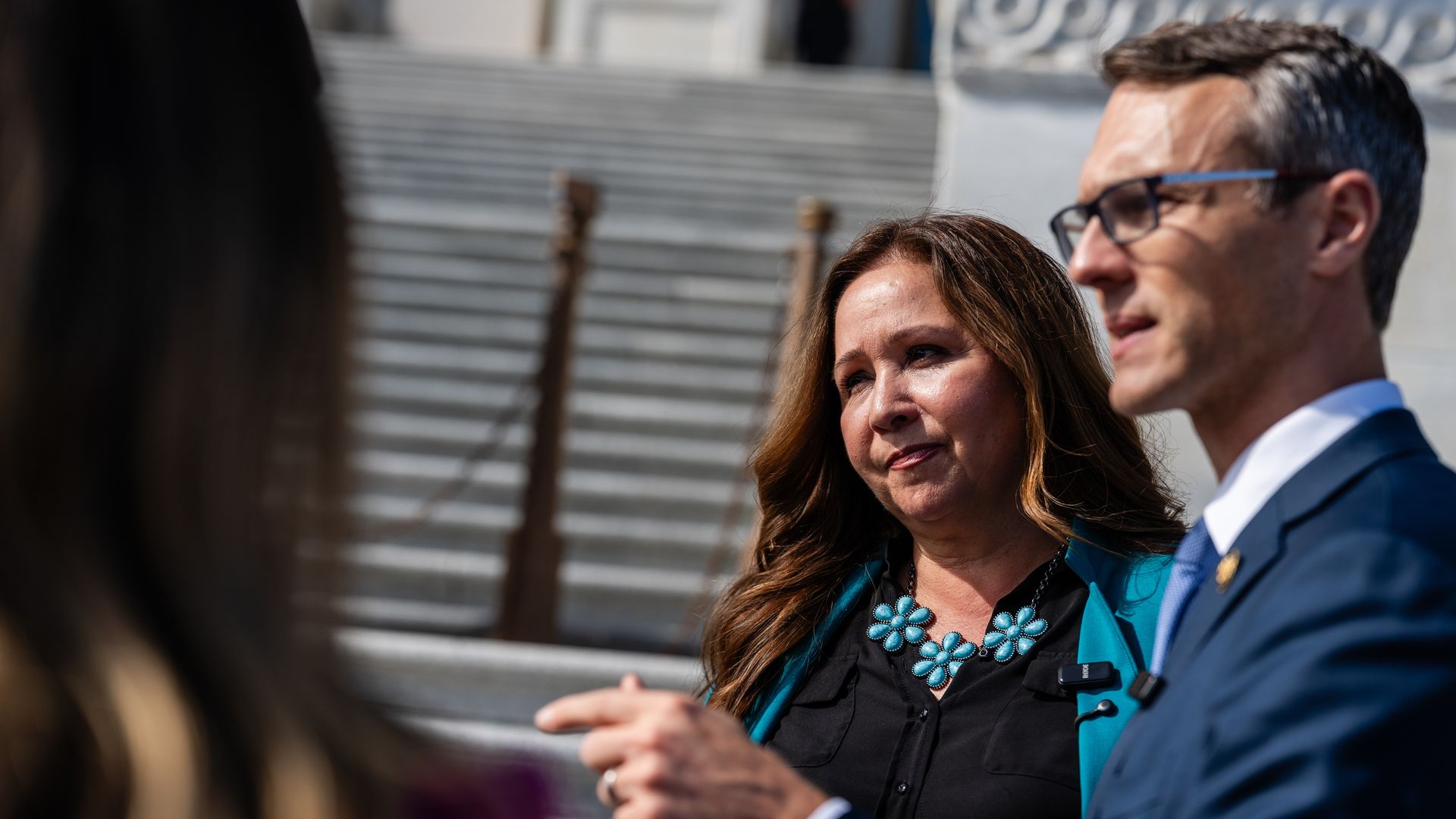 Adelita Grijalva, wearing a turquoise necklace and matching blazer, stands next to James Walkinshaw as he speaks in front of the U.S. Capitol building.