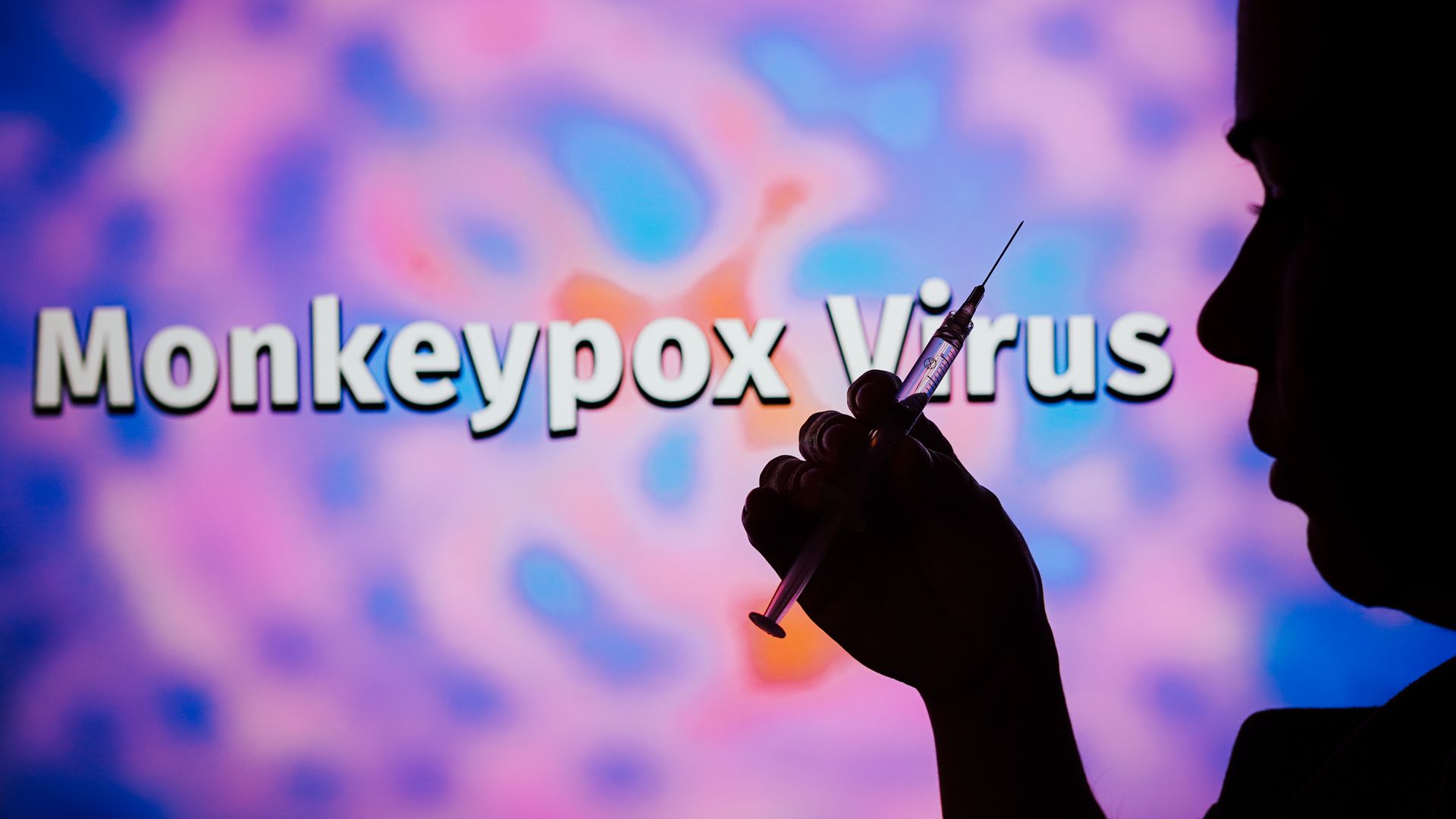 A  silhouetted man holding a medical syringe with the word Monkeypox virus in the background. 