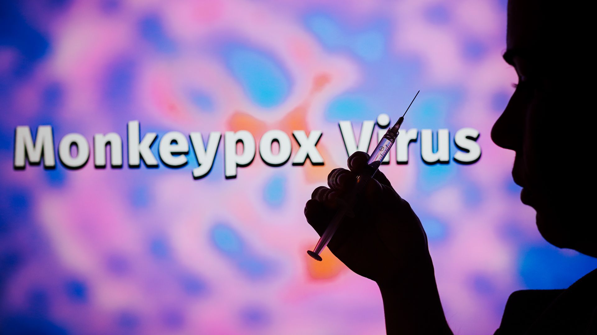 A silhouetted man holding a medical syringe with the word Monkeypox virus in the background.