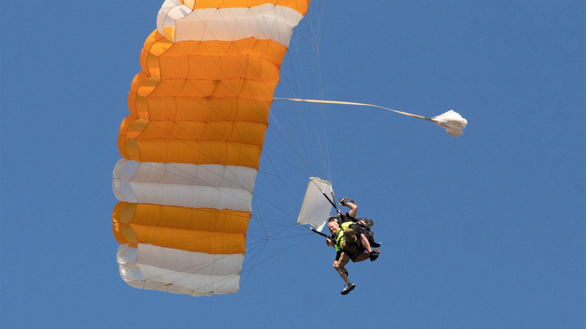 George Downing descends with a yellow-and-white parachute from the sky after skydiving.