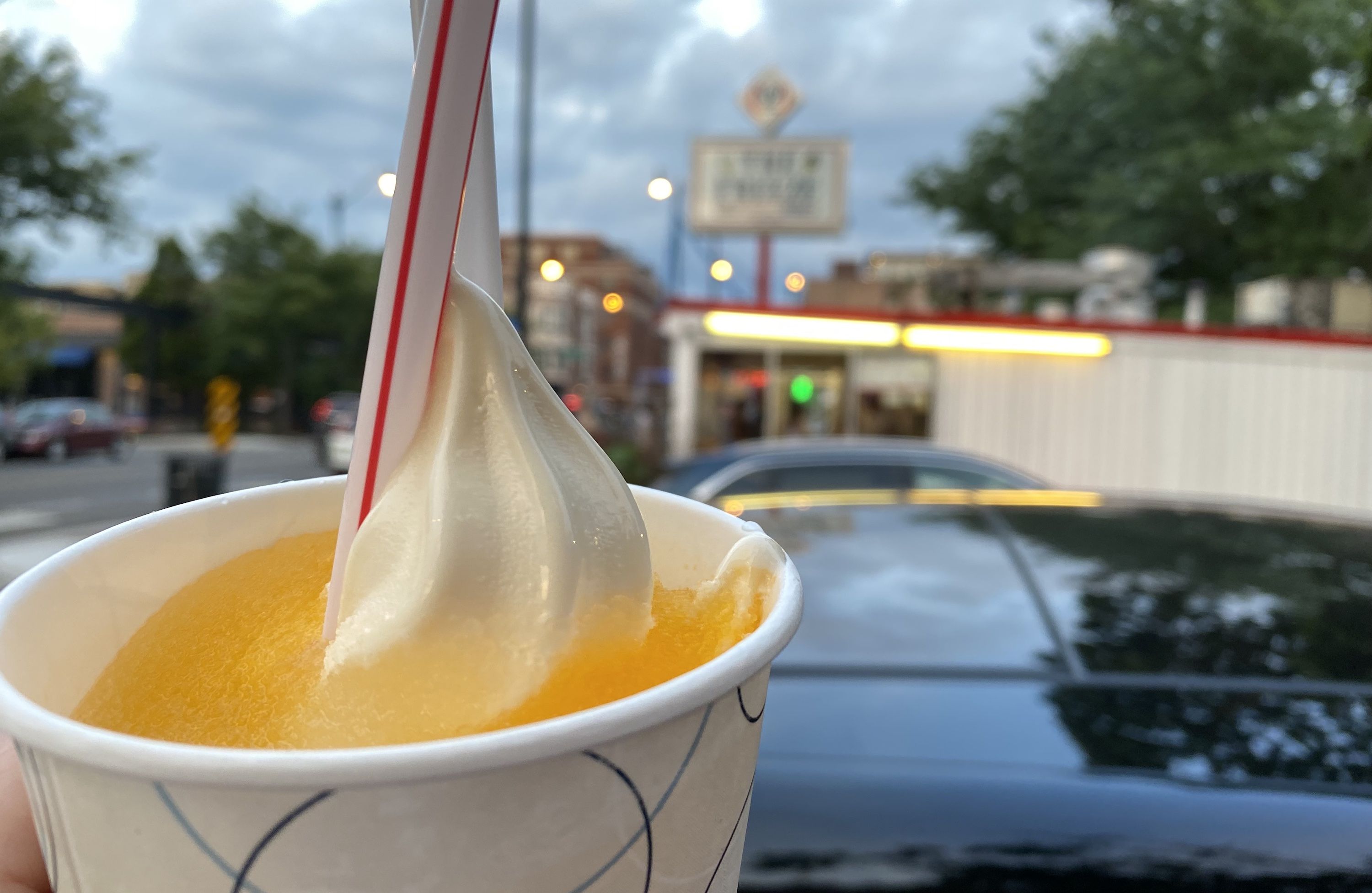 Paper cup with orange slushie, vanilla ice cream and striped straw.