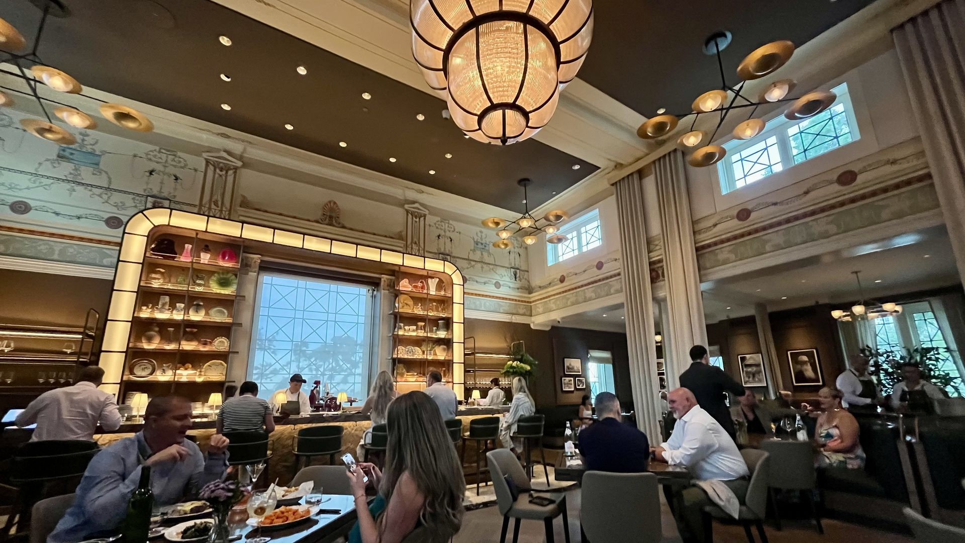 A dining room with decorated walls, chandeliers sand a bar.
