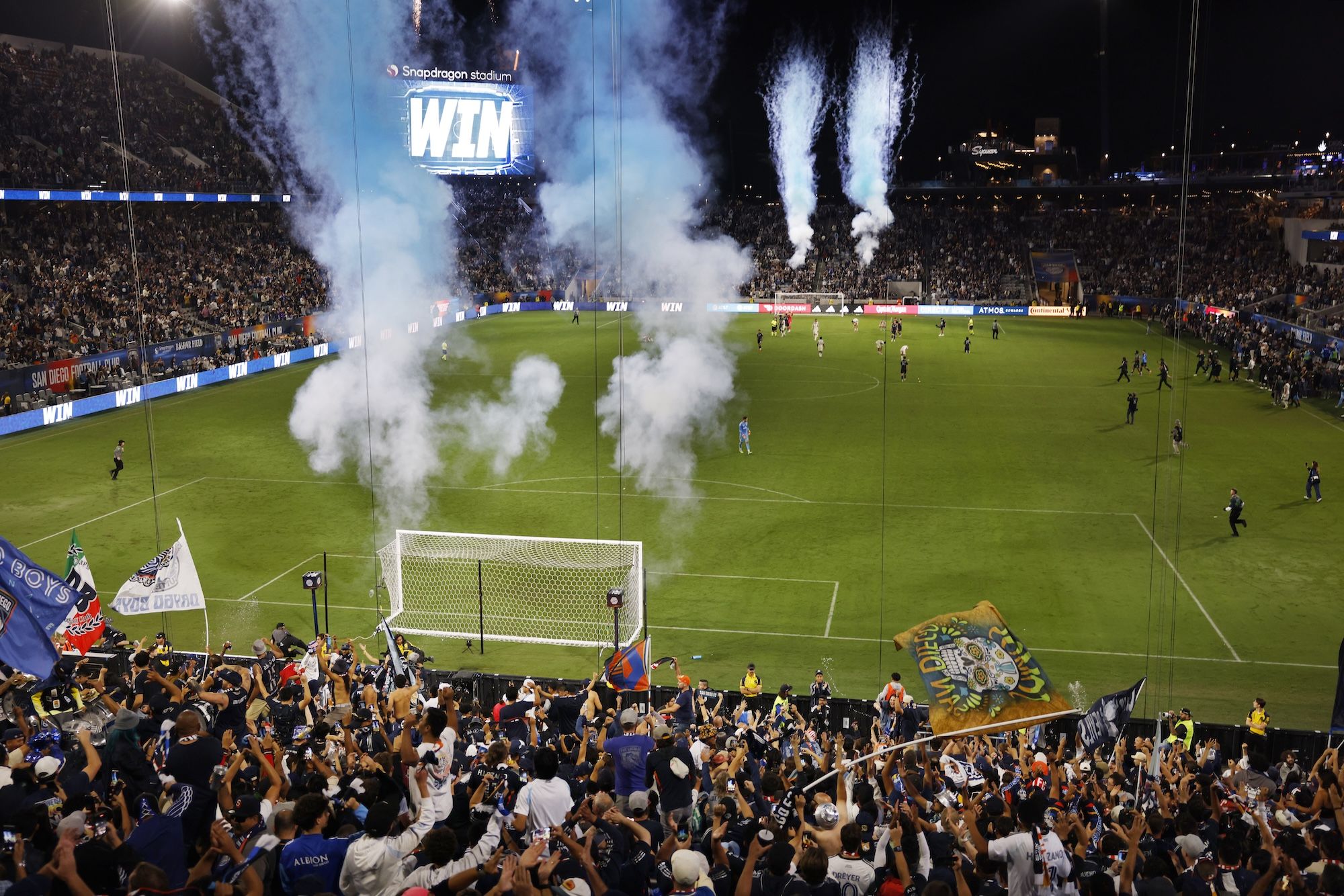 Blue smoke shoots out from behind two soccer goals on opposite sides of the field as fans cheer in Snapdragon Stadium.