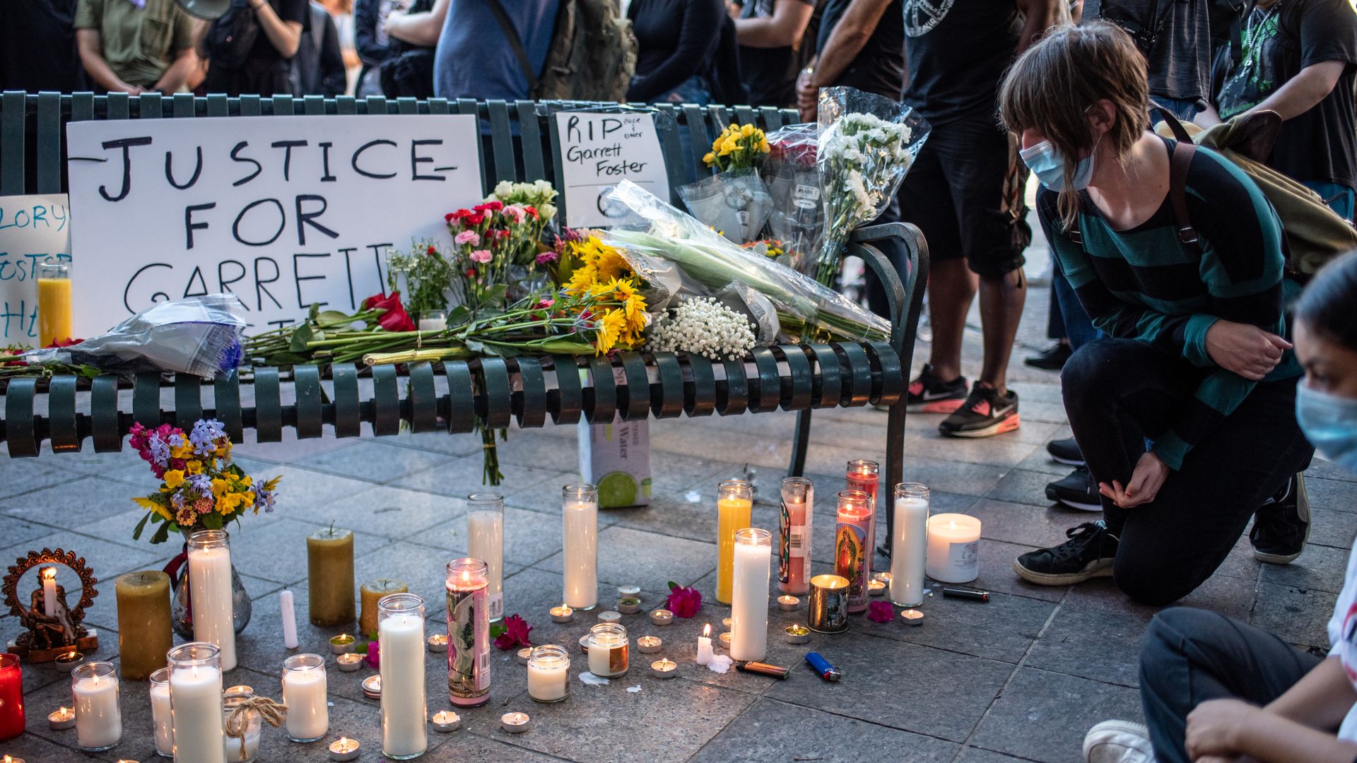 A makeshift memorial on a bench. A poster reads "JUSTICE FOR GARRETT" and lit candles dot the pavement below.