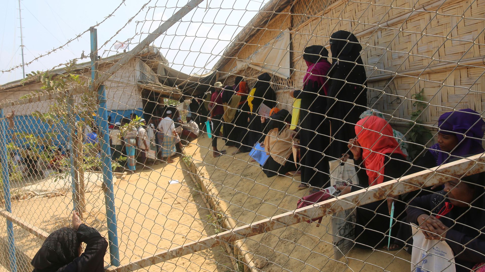 In this image, people behind a fence stand in line outside 