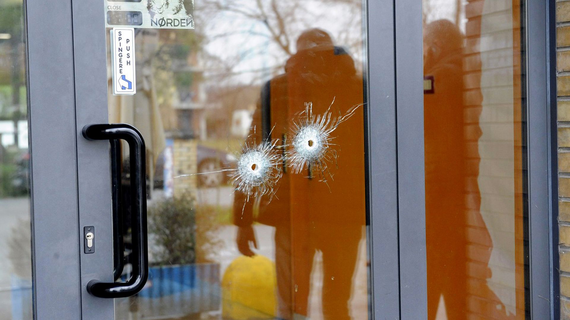 Bullet holes are seen in a glass door following a drive-by shooting at Macerata.