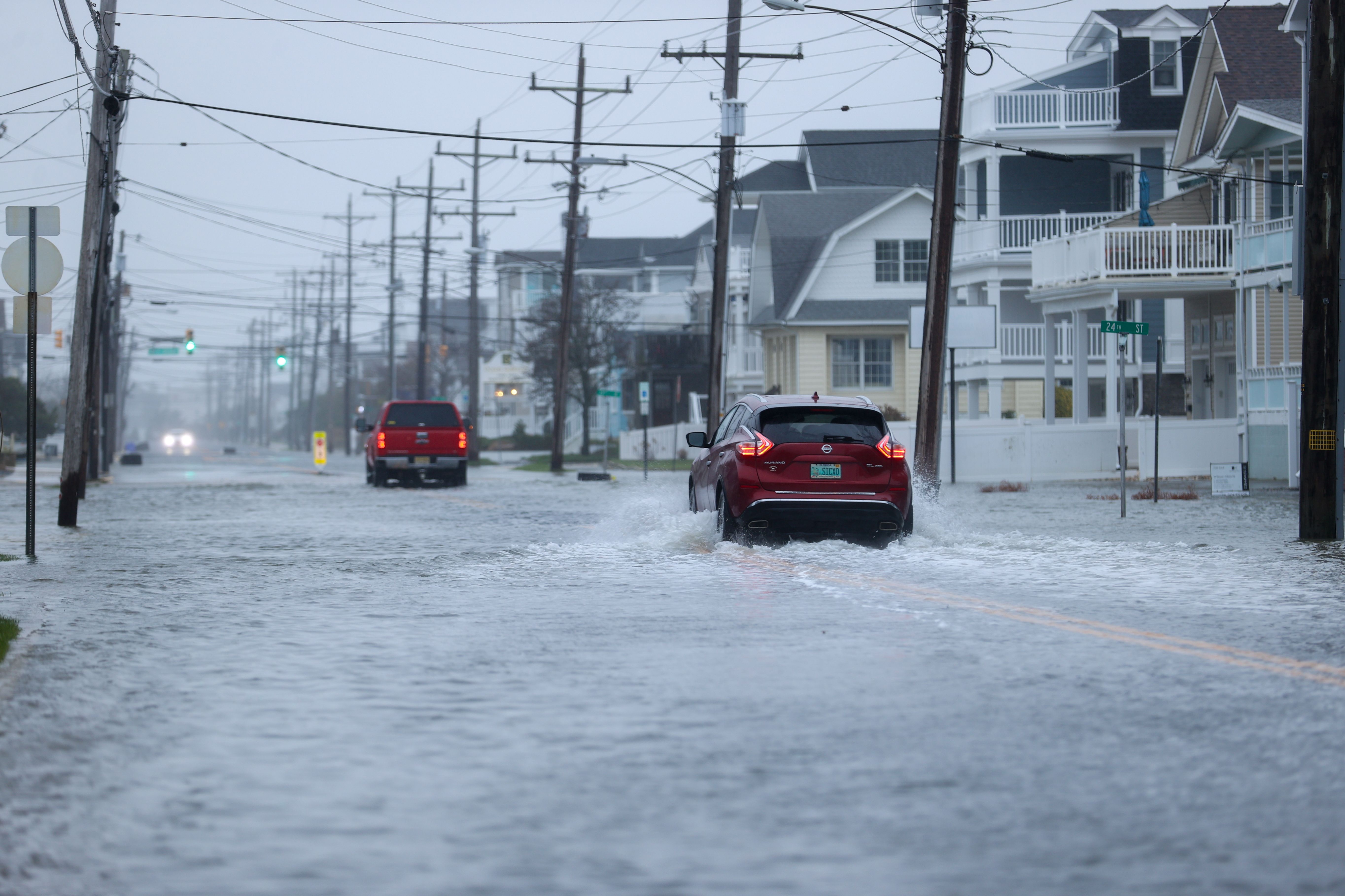 Two red cars drive through a flooded street filled with brown and white apartments and surrounded by brown power lines in Avalon, New Jersey, on October 12.