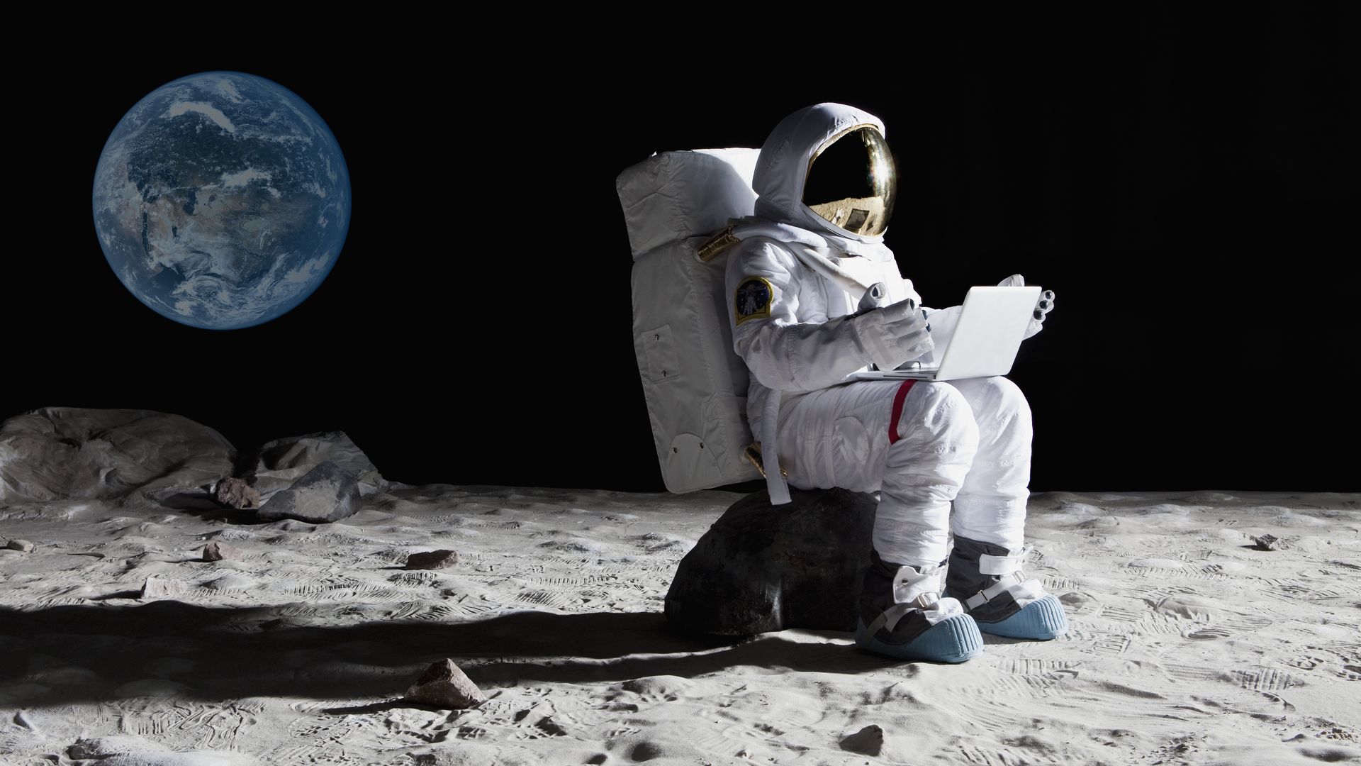 Man uses laptop on the moon.