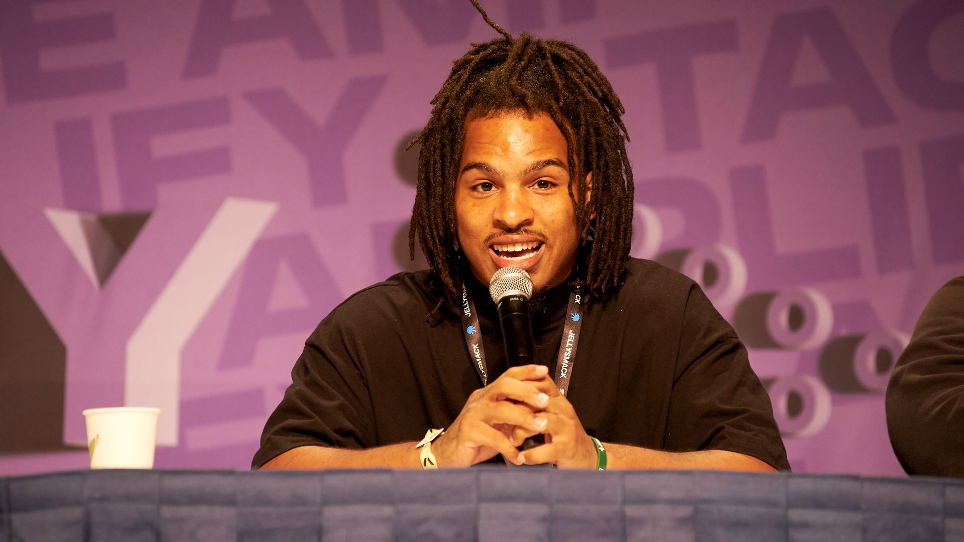 Keith Lee with a microphone in hand in front of a purple background