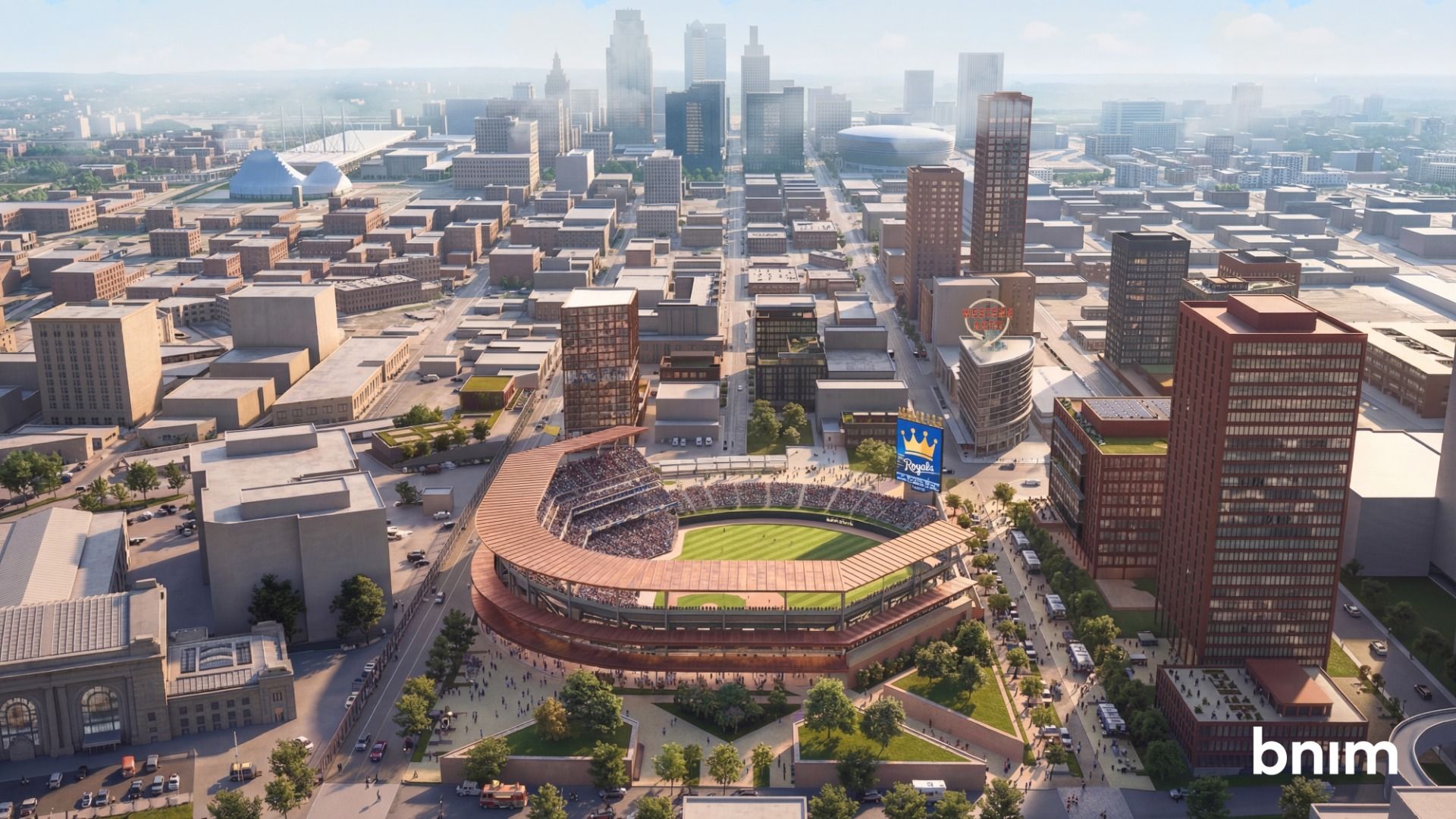 Aerial view of Kansas City with a large baseball stadium in the foreground. Copper-orange seating encircles the oval field; surrounding high-rise blocks and a bright sky, with a Royals scoreboard.