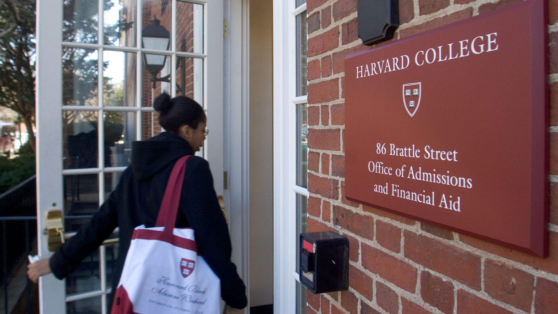 A student with a red and white Harvard tote bag walks into the Office of Admissions and Financial Aid.