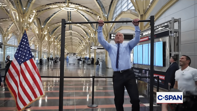 RFK Jr. demonstrates pull-ups at Reagan National Airport in a button down shirt and tie and slacks. 