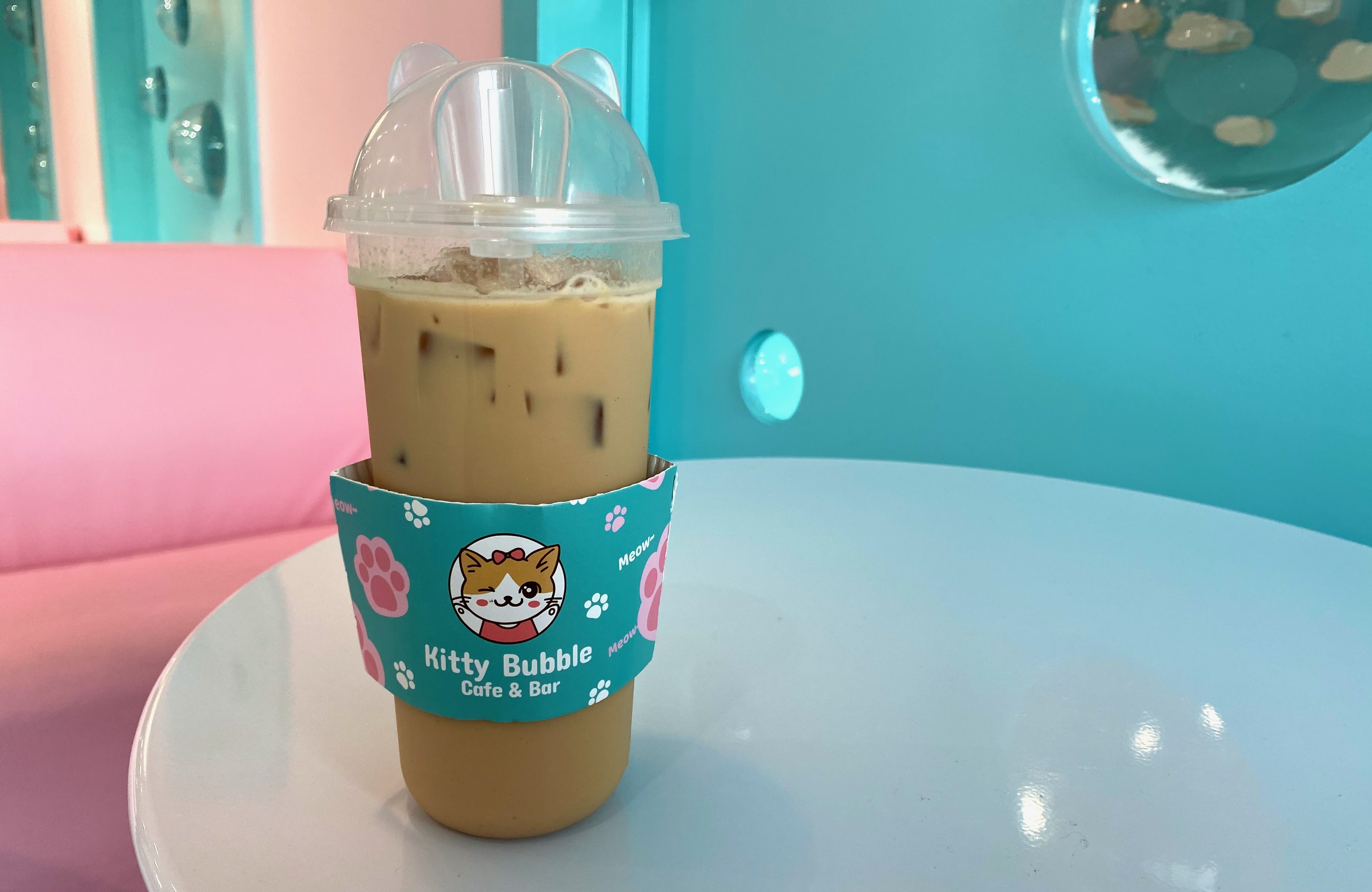 A plastic coffee cup with cat ears on top and a "Kitty Bubble Cafe & Bar" sleeve on it